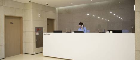 A reception desk in a modern lobby with a marble wall, a security camera, and a fire alarm.