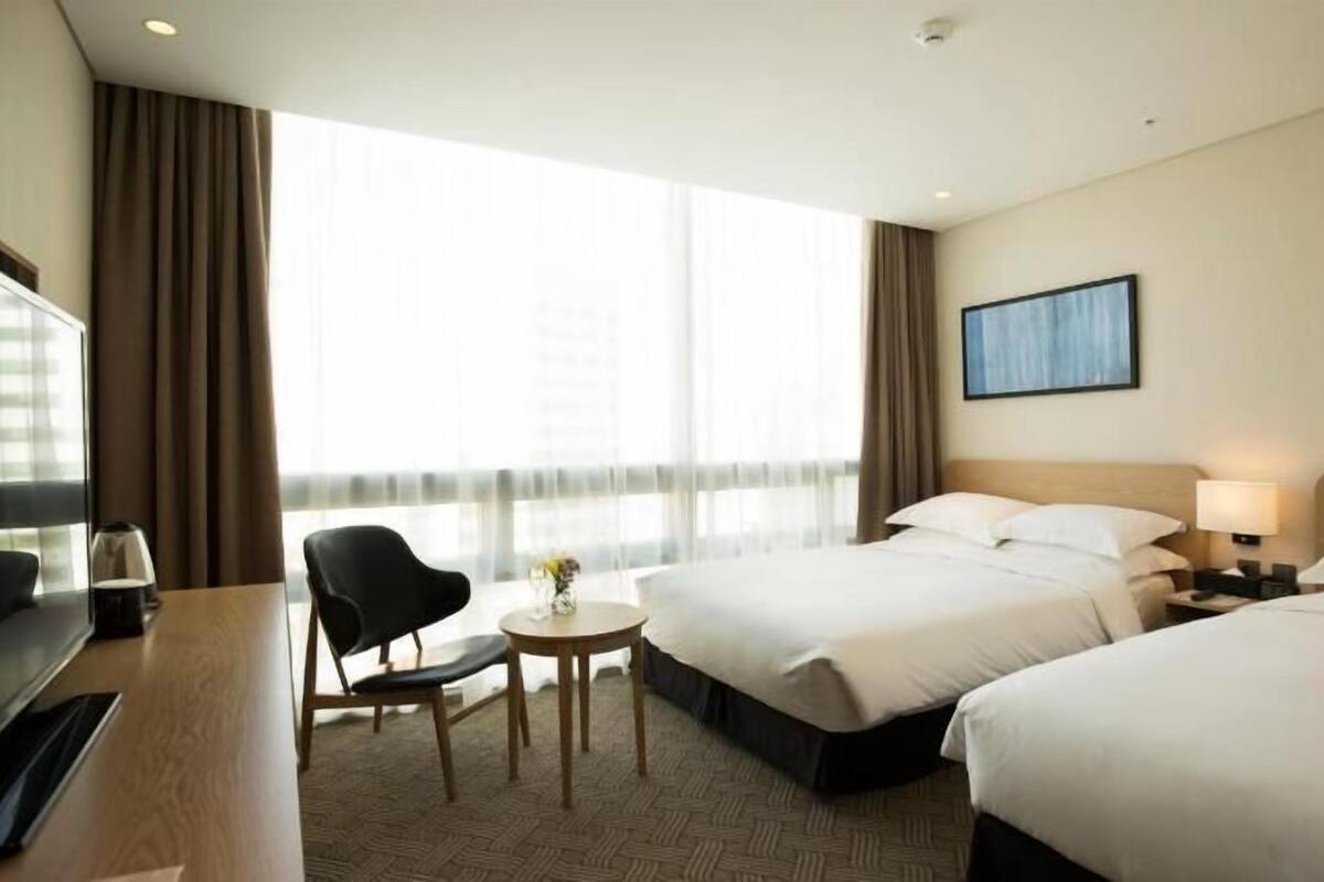 A hotel room with two beds, a desk, a chair, a TV, and a window with curtains.