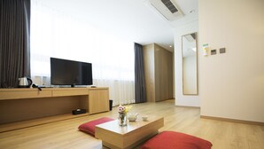 A modern hotel room with a wooden floor, a flat-screen TV, a coffee table with a vase of flowers, and red cushions. - Best Western Haeundae Hotel (Busan)