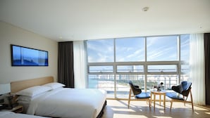 A hotel room with a large bed, a desk with a chair, and a view of the city through large windows. - Best Western Haeundae Hotel (Busan)