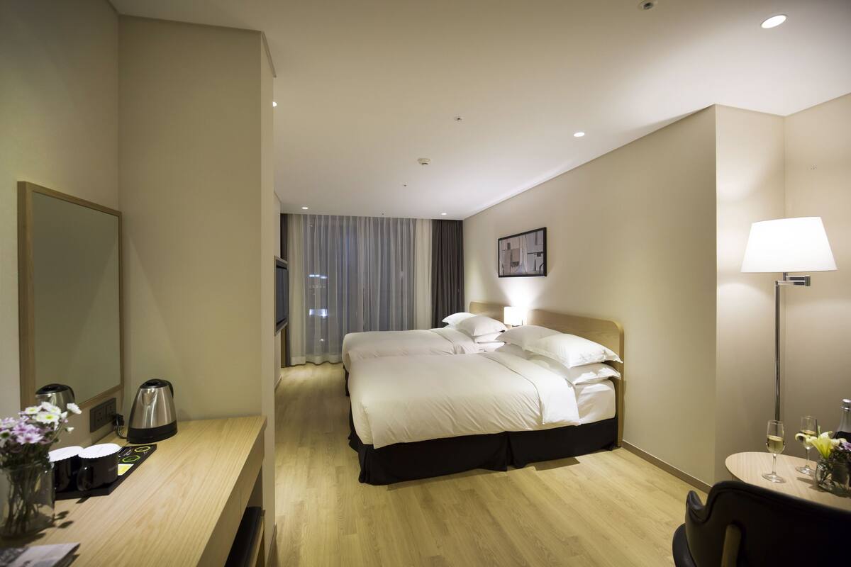 A hotel room with a bed, bedside table, lamp, and a view of the city through the window.