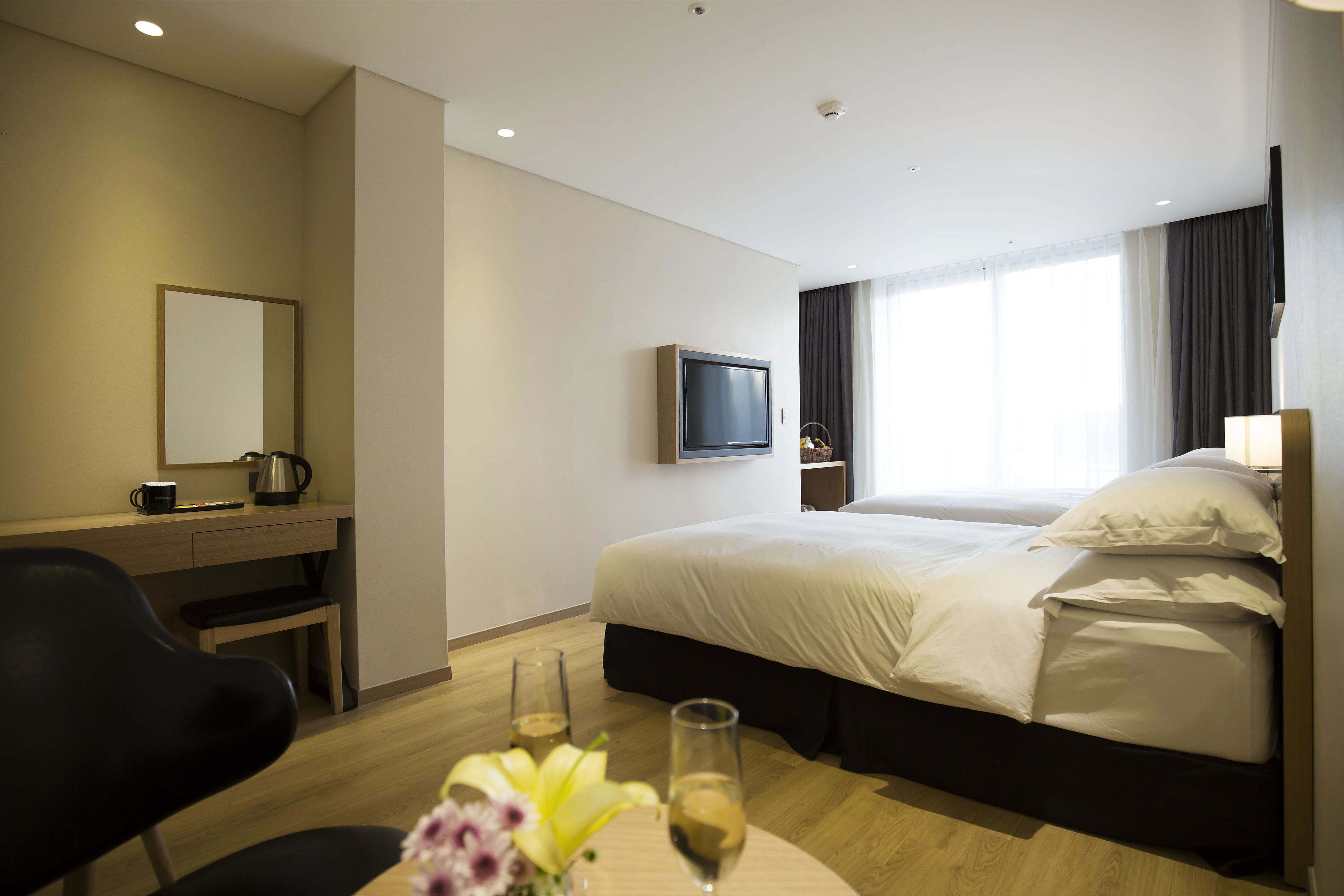 A hotel room with a bed, a desk with a chair, a television, and a window with curtains.
