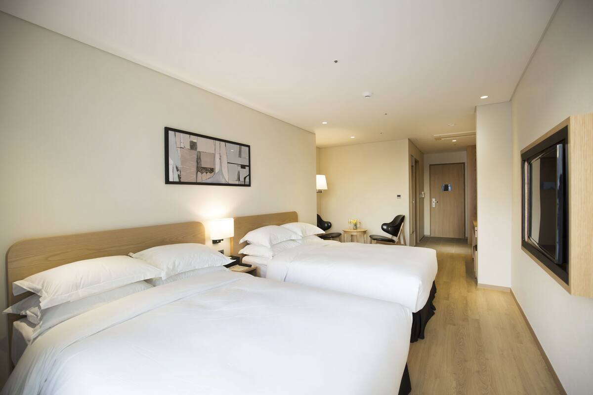 A hotel room with two beds, a nightstand, a lamp, a chair, and a framed picture on the wall.