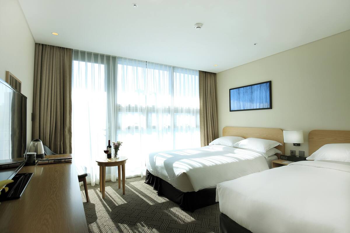 A hotel room with a large bed, a desk with a chair, a small table with a lamp, and a TV.