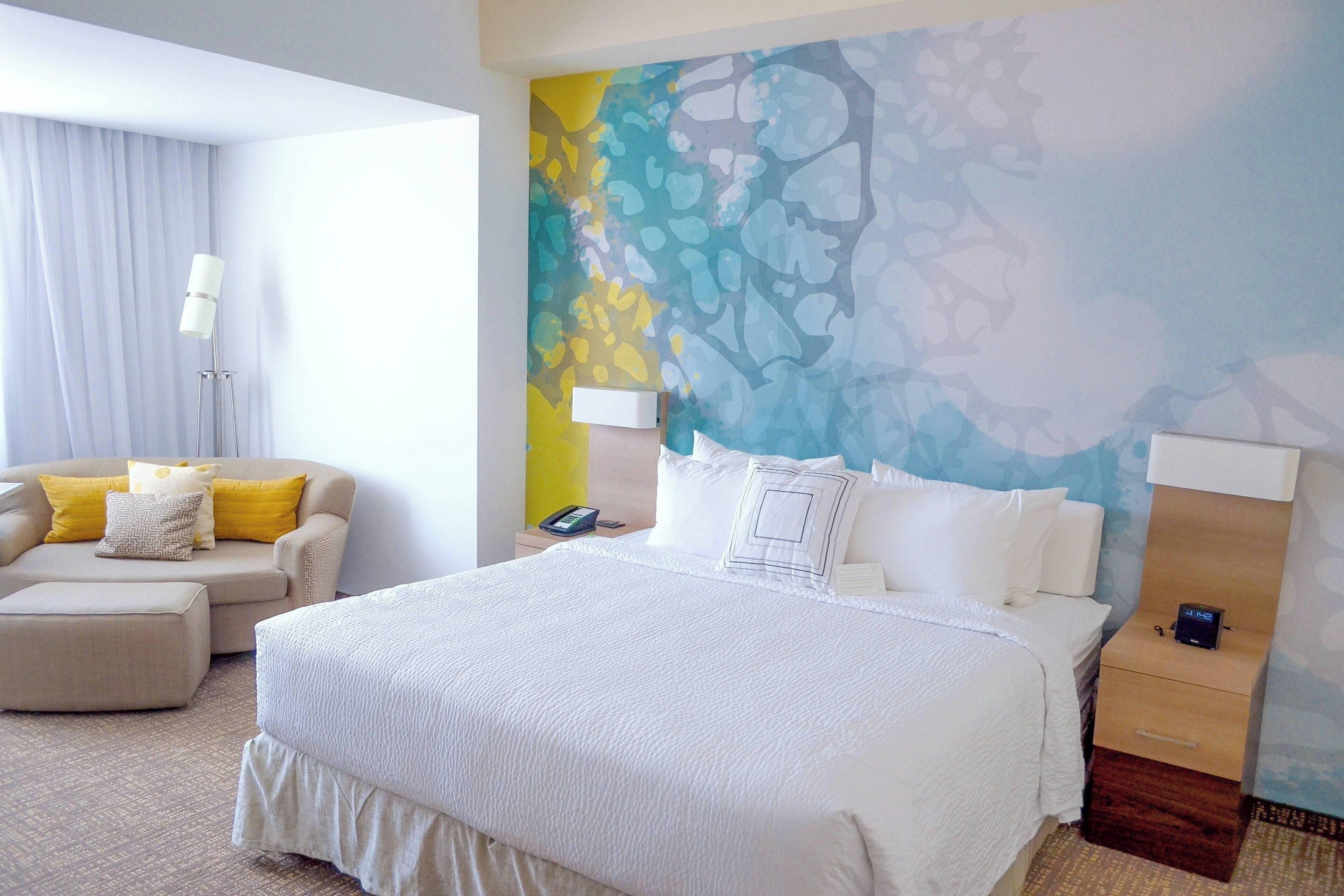A hotel room with a large bed, a sofa, a nightstand, and a wall with a colorful abstract design.