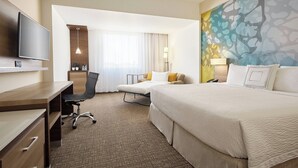 Une chambre d’hôtel avec un lit, un bureau, une chaise, une télévision et un tableau au mur.