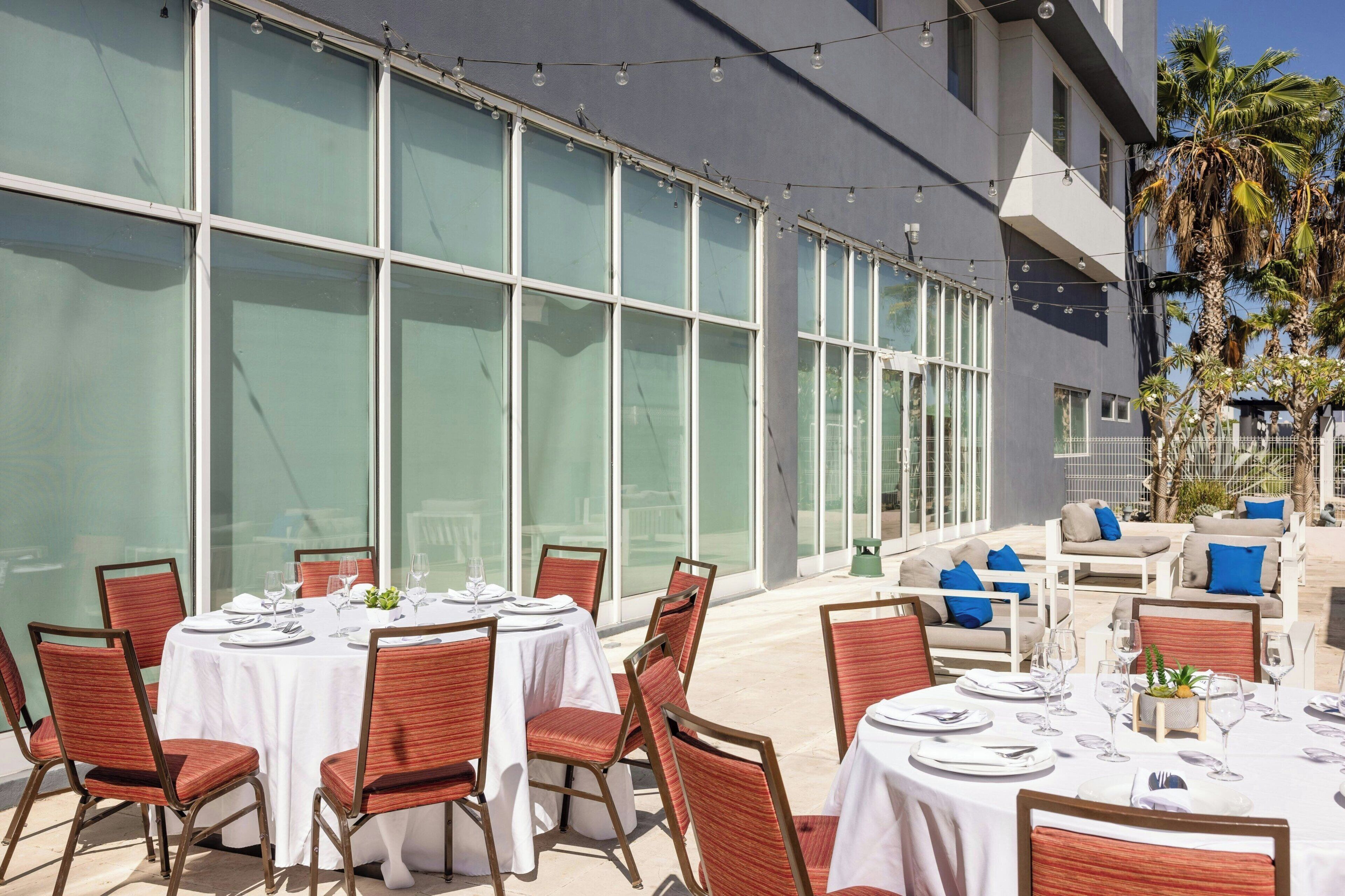 Un espace de restauration en plein air avec des tables rondes disposées pour accueillir quatre personnes, entourées de chaises en osier.