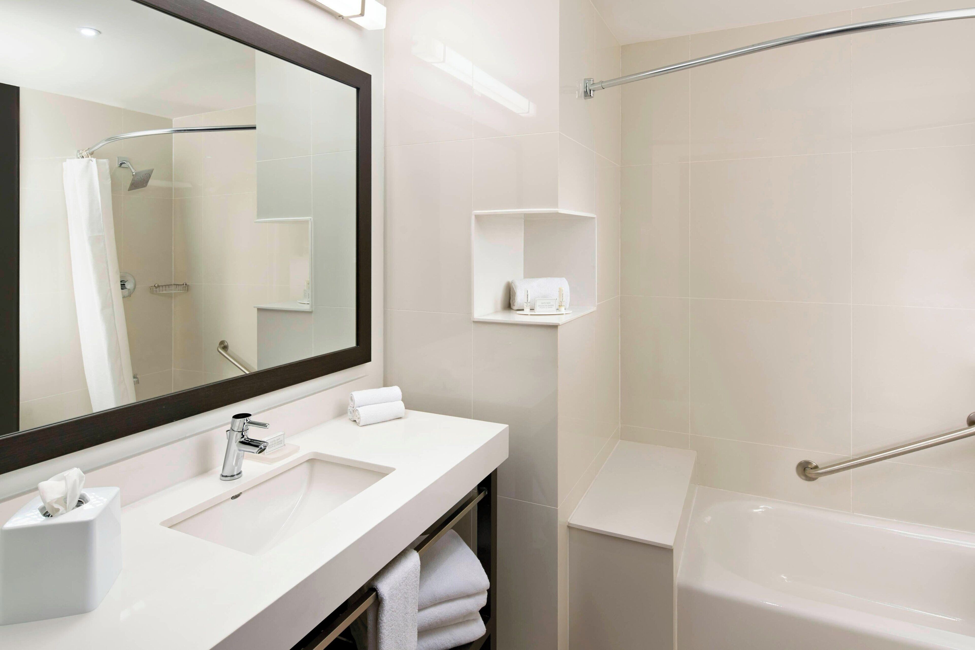 A modern bathroom with a large mirror, two sinks, a bathtub, and a shower.