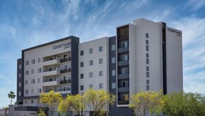 Un hôtel Courtyard by Marriott au design moderne, doté de nombreux balcons et offrant une vue sur un ciel dégagé.