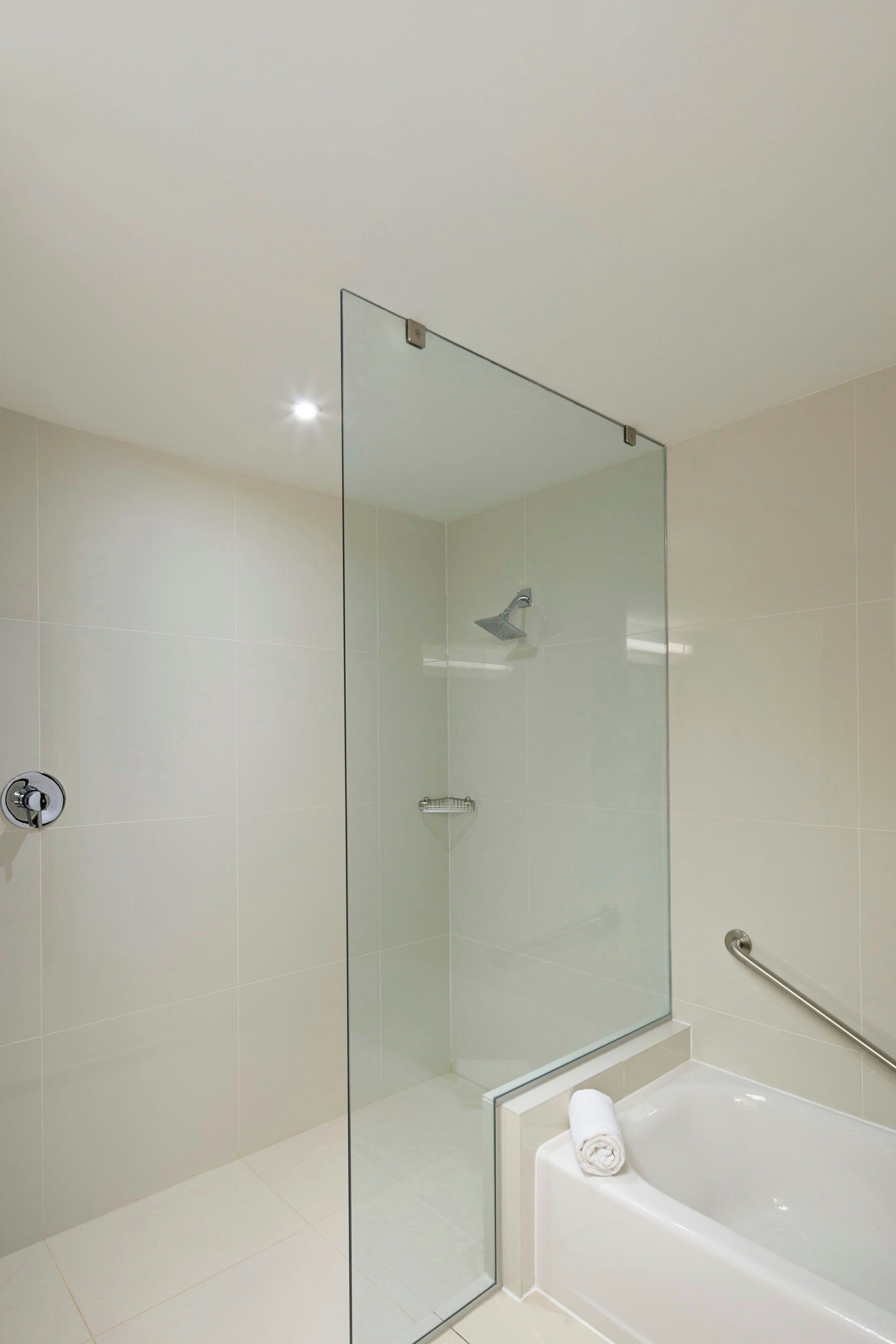 Un baño moderno con cabina de ducha de vidrio, bañera de hidromasaje y pasamanos para facilitar el acceso.