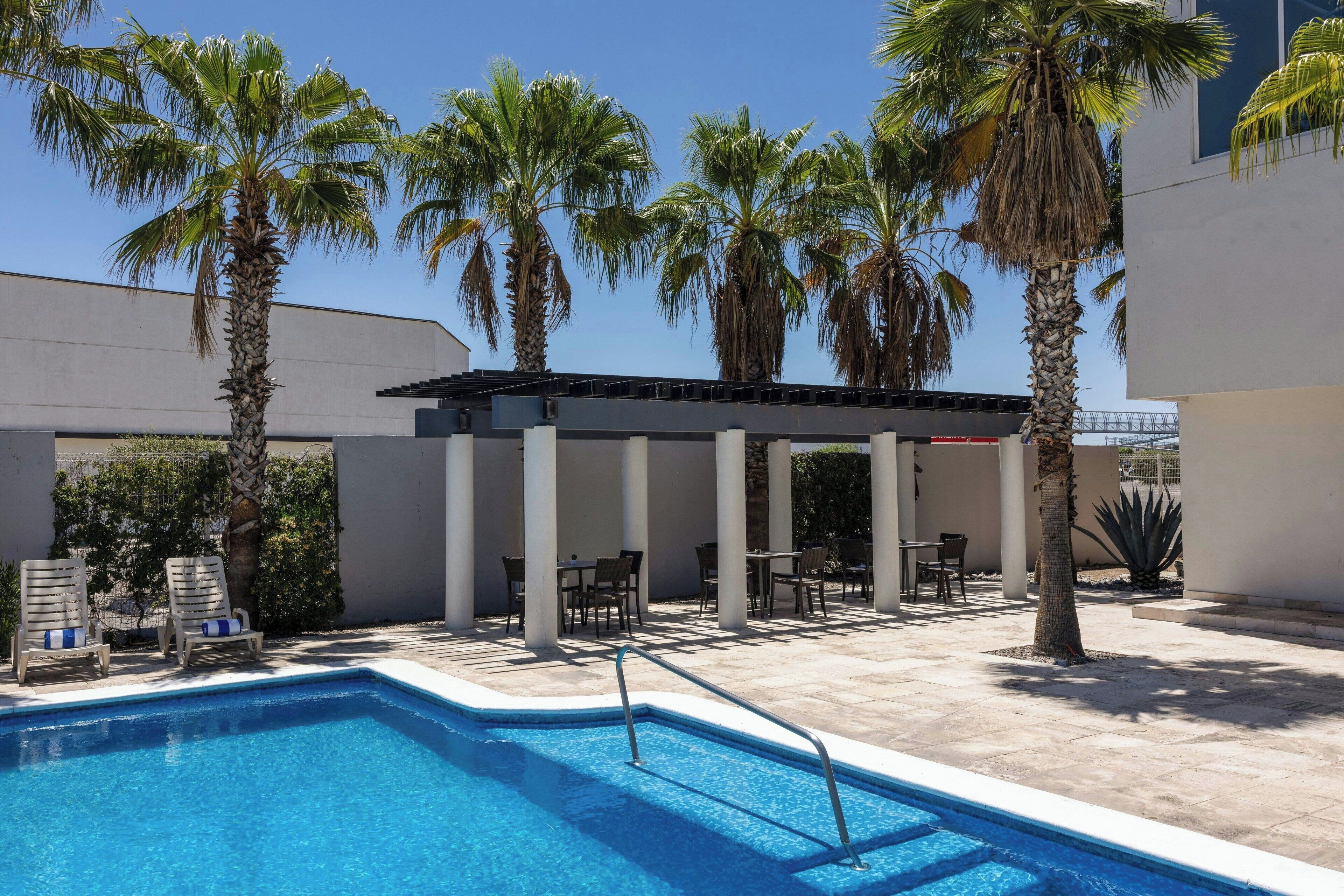 A swimming pool with lounge chairs and palm trees.