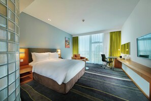 A hotel room with a large bed, a desk, a chair, and a TV.
