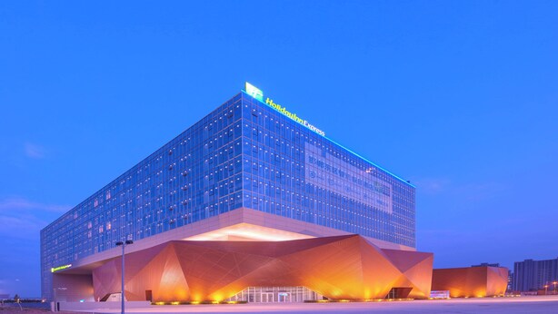 A modern hotel building with a prominent glass facade and a unique architectural design featuring a large, angular entrance.