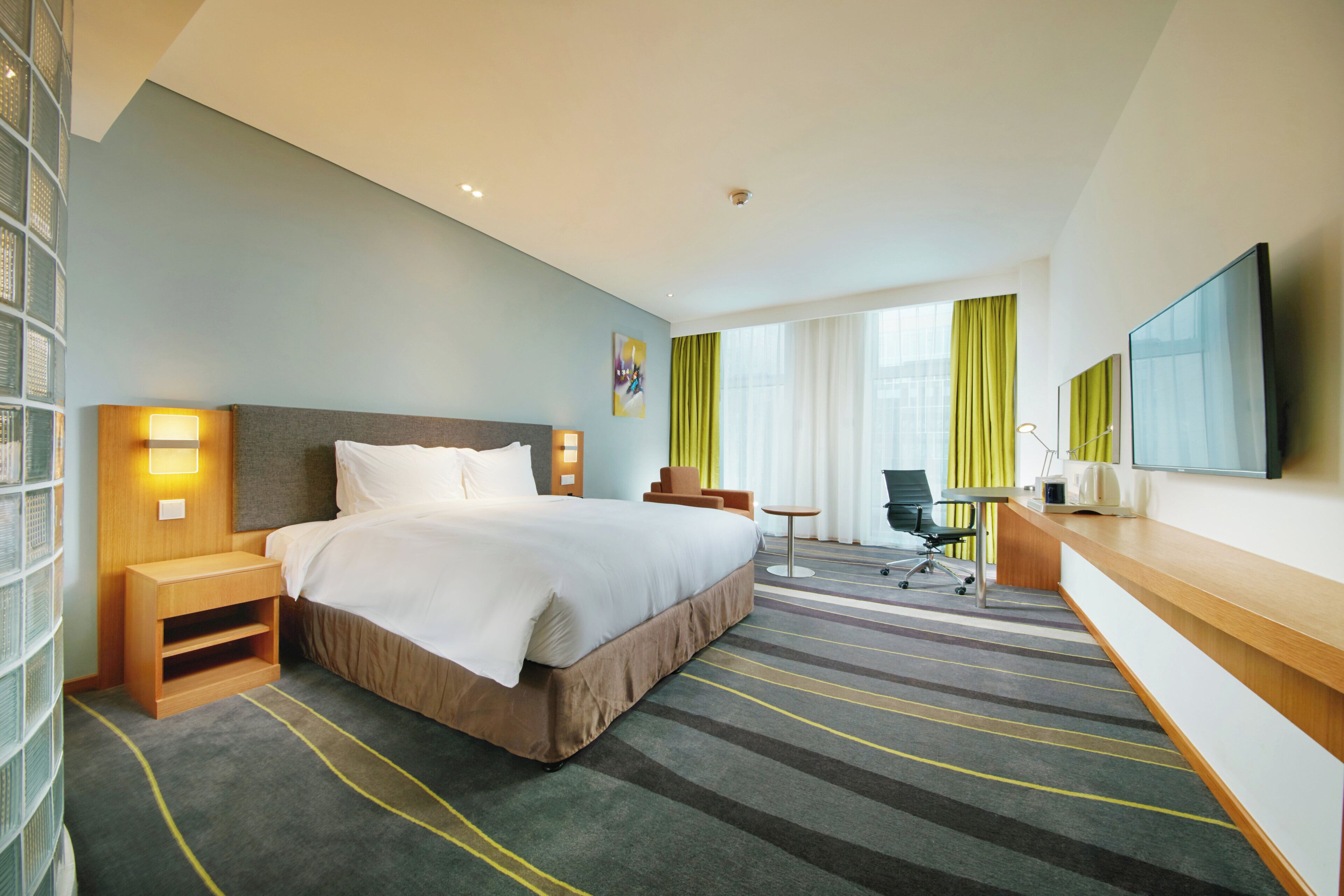 A hotel room with a bed, bedside tables, a desk, a chair, a TV, and a window with curtains.