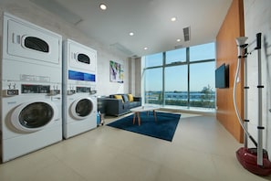 A laundry room with stacked washing machines, a gray sofa with yellow pillows, and a large window offering a city view. - Holiday Inn Express Handan East by IHG (Handan)