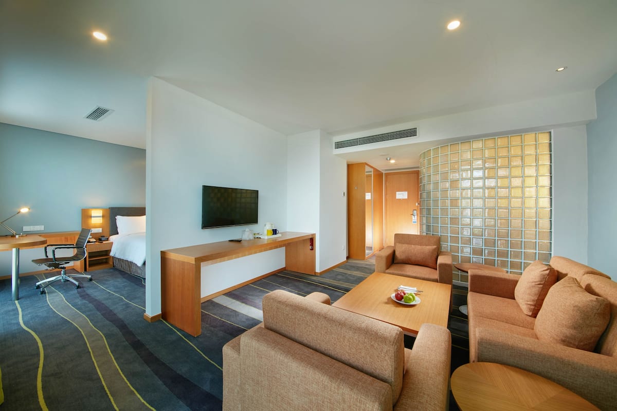 A modern hotel room with a flat-screen TV, a desk with a chair, a sofa set, and a large window with a view.