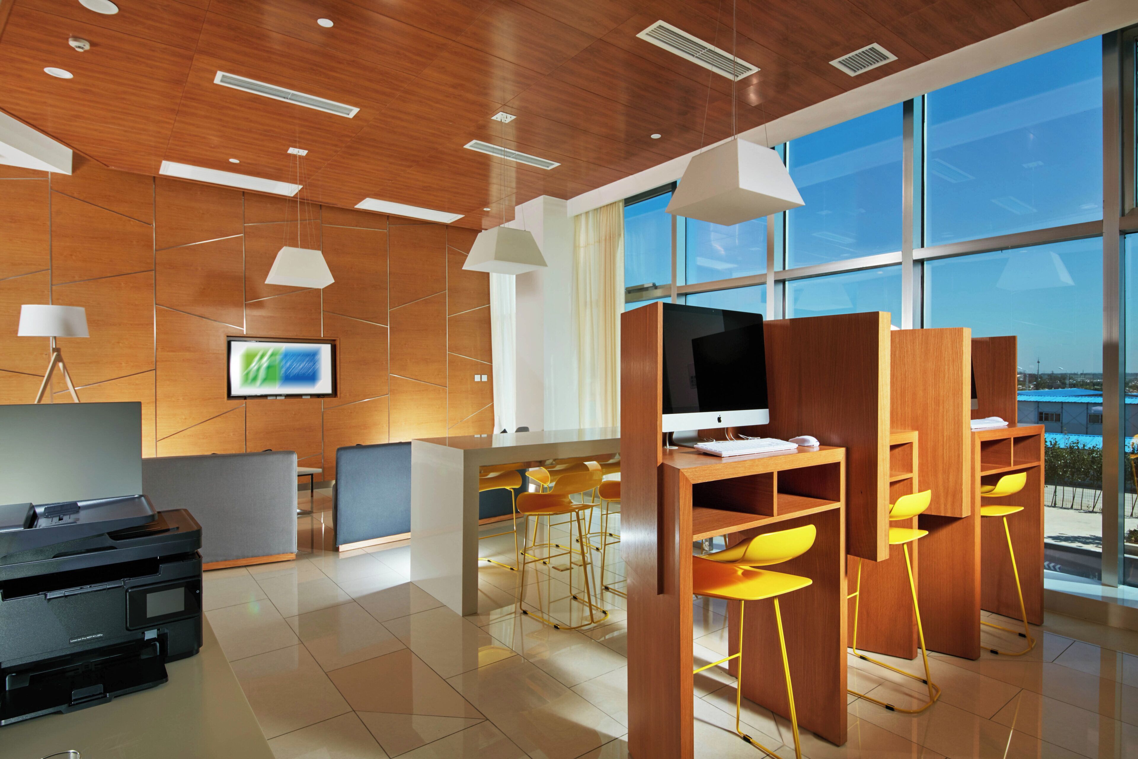 Un espacio de oficina moderno con techo de madera, ventanas amplias y una zona de escritorio con computadora y sillas.