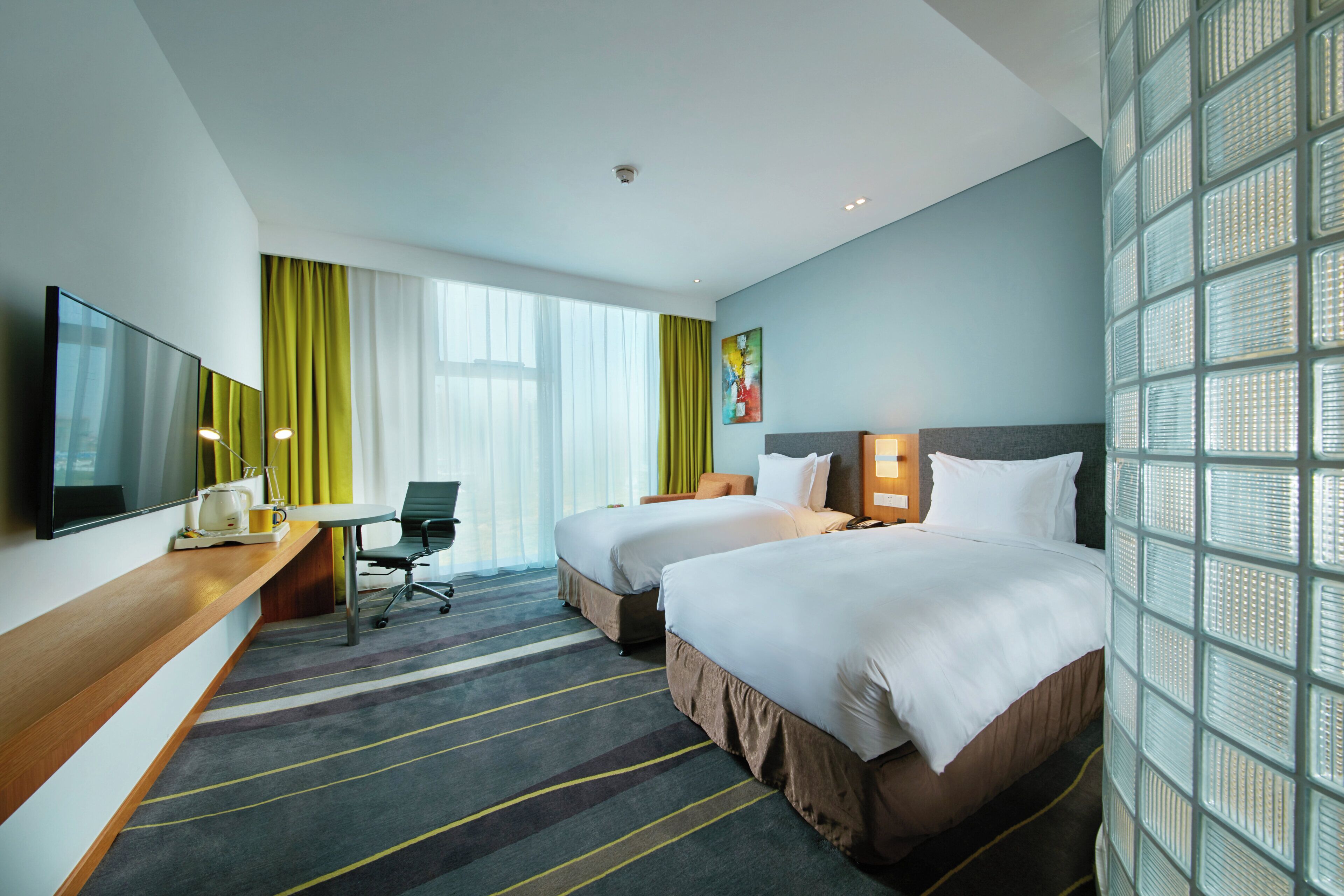 A hotel room with two beds, a desk with a flat-screen TV, a chair, a coffee maker, and a window with curtains.