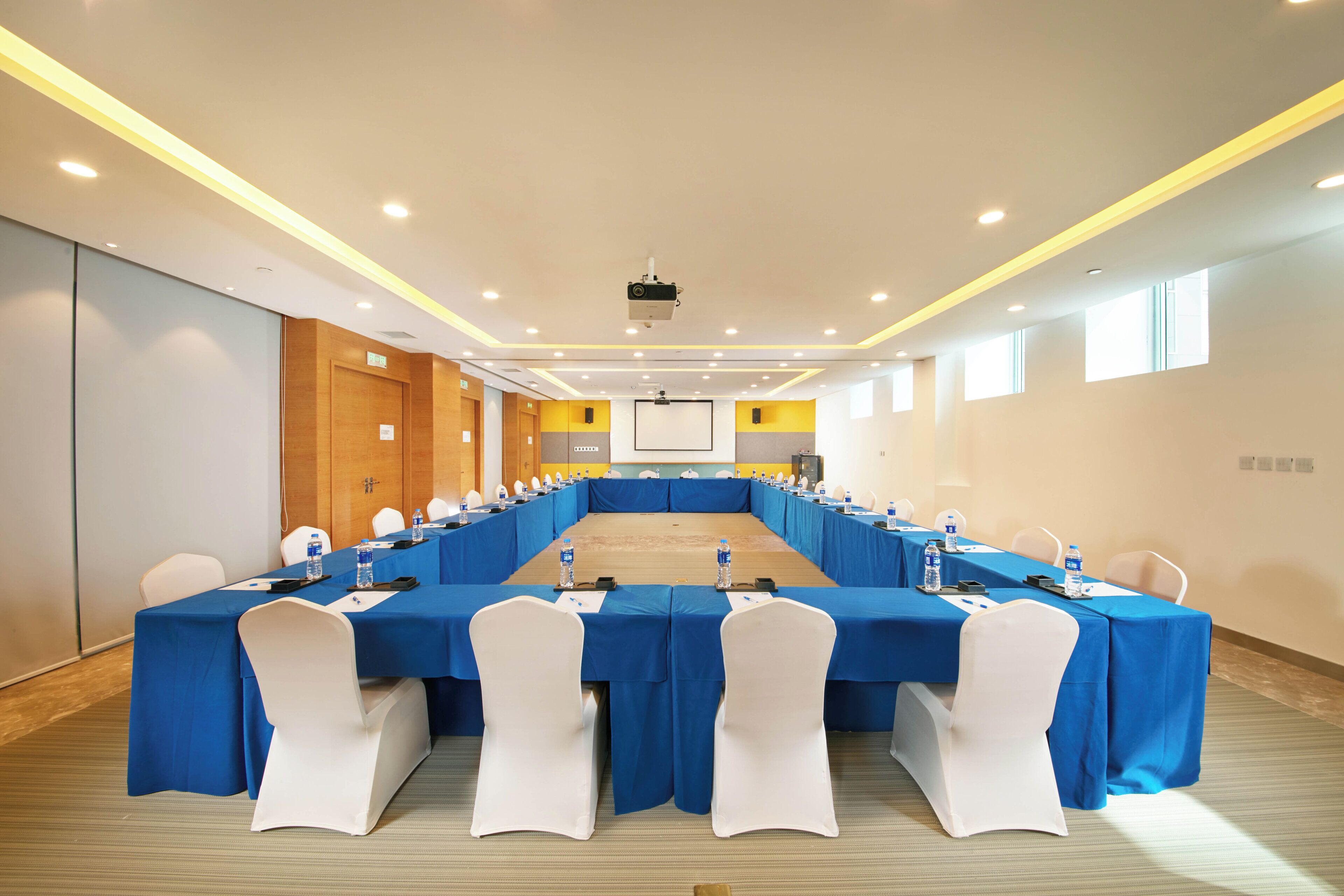 A conference room with a long table, white chairs, and blue tablecloths.