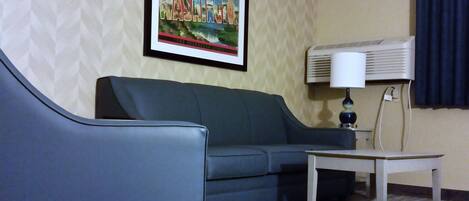 A hotel room with a green sofa, a small table, and a framed picture on the wall.