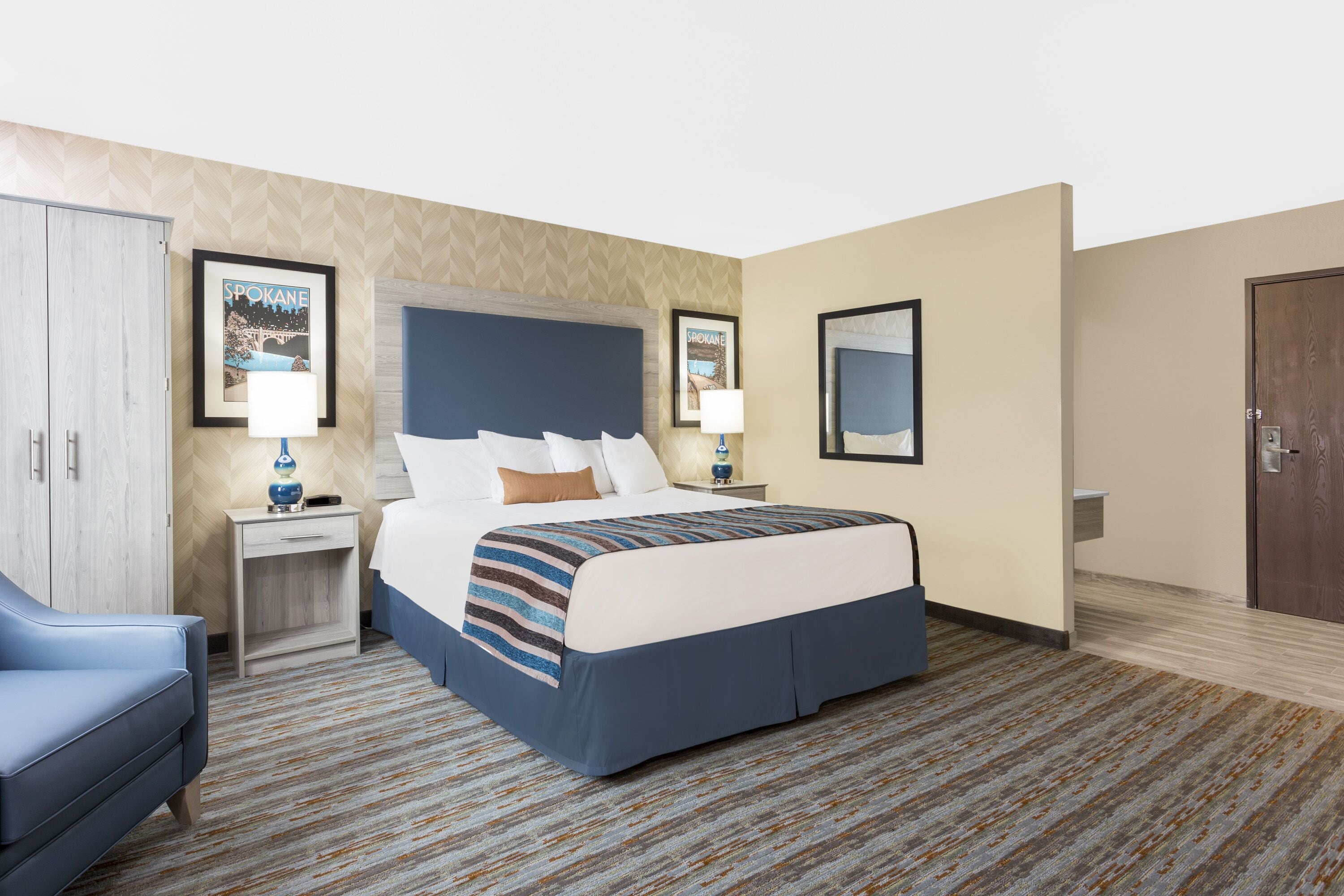 A hotel room with a large bed, a desk, a chair, and a wardrobe.