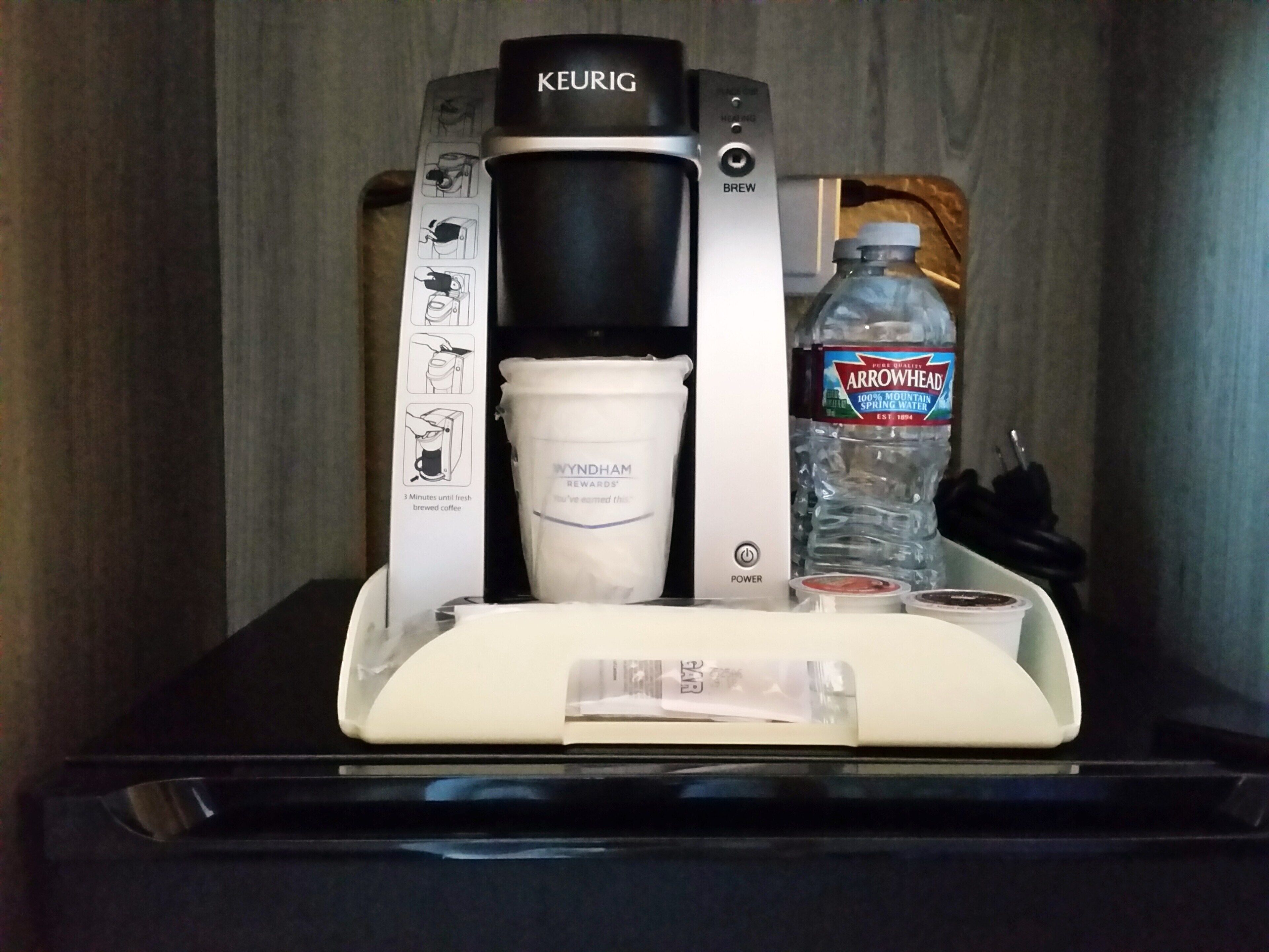 Una cafetera Keurig con portavasos, una botella de agua y una cápsula de café.