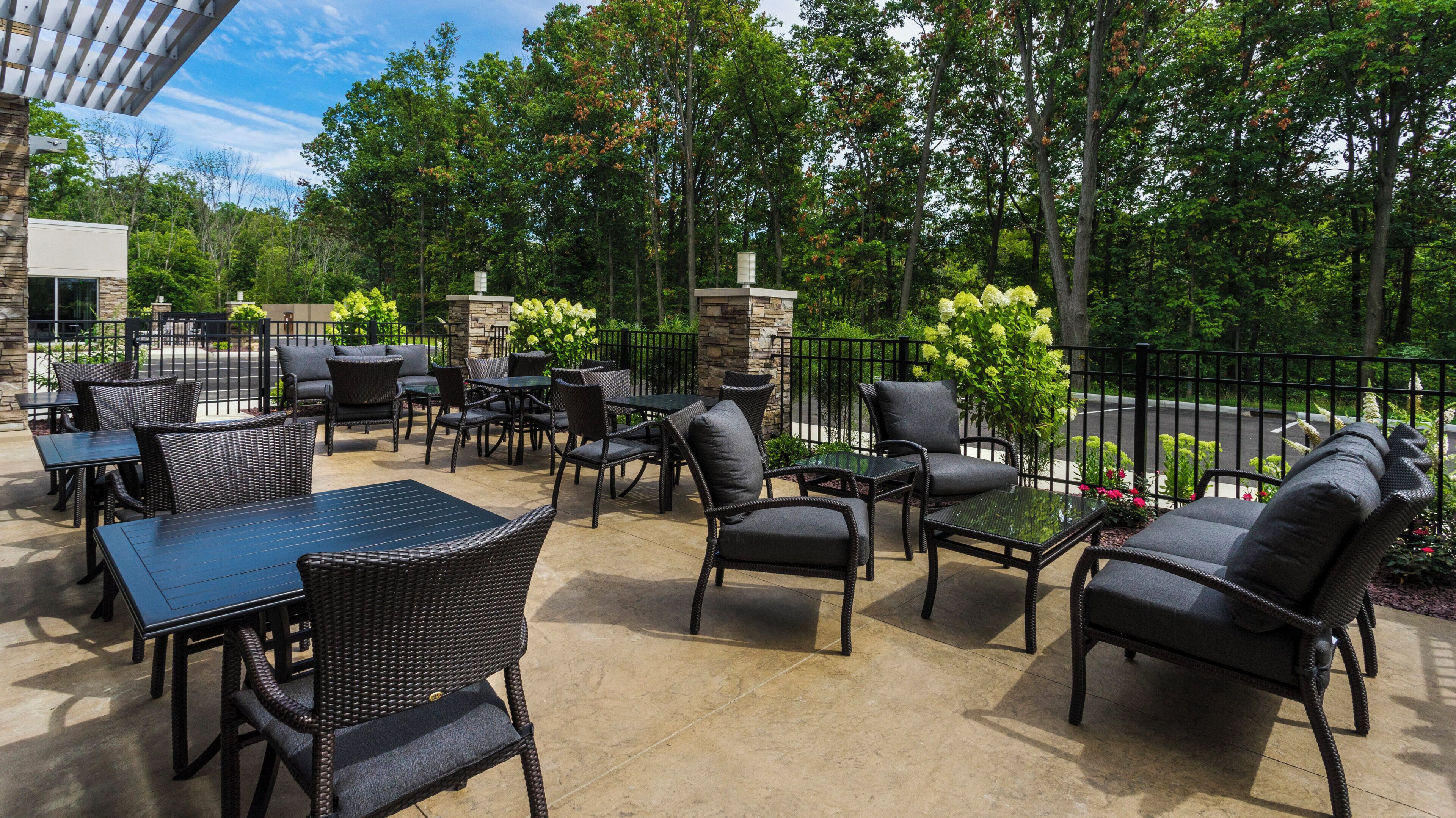 An outdoor patio area with tables and chairs, surrounded by a stone wall and greenery.