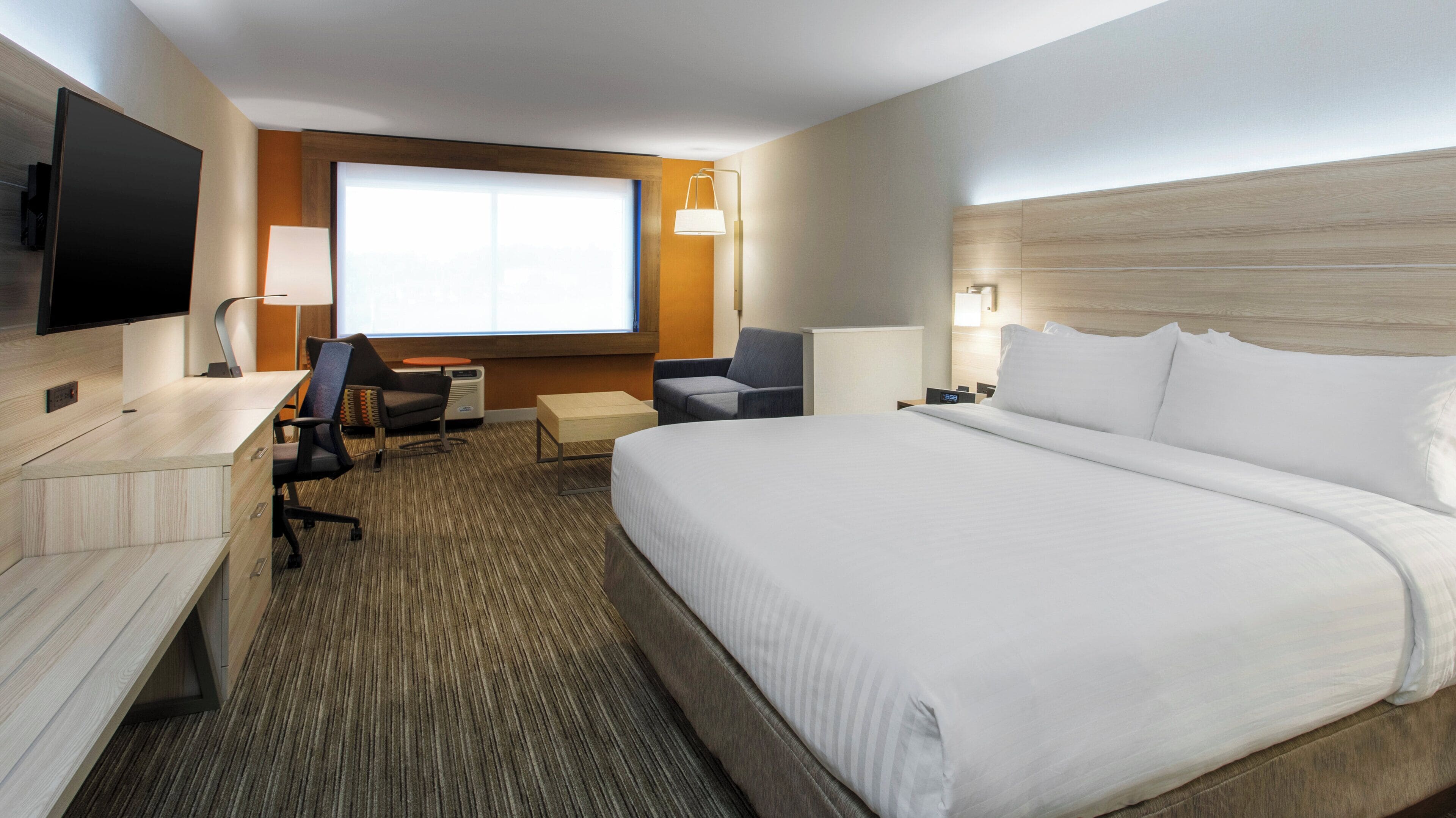 Een hotelkamer met een groot bed, een bureau met een stoel, een televisie en een raam met uitzicht.