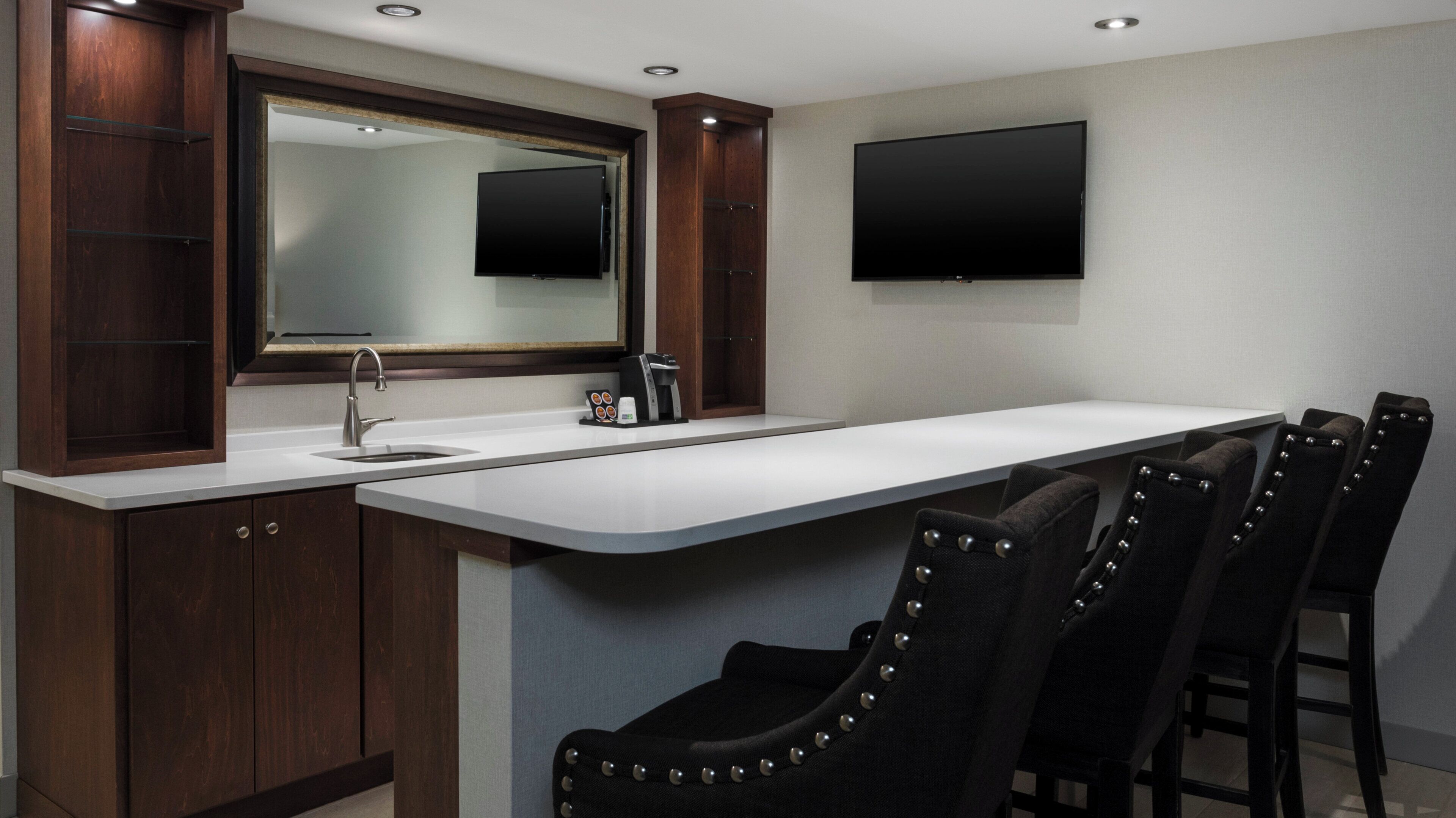 A modern kitchen with a built-in sink, a large mirror, and a flat-screen TV mounted on the wall.
