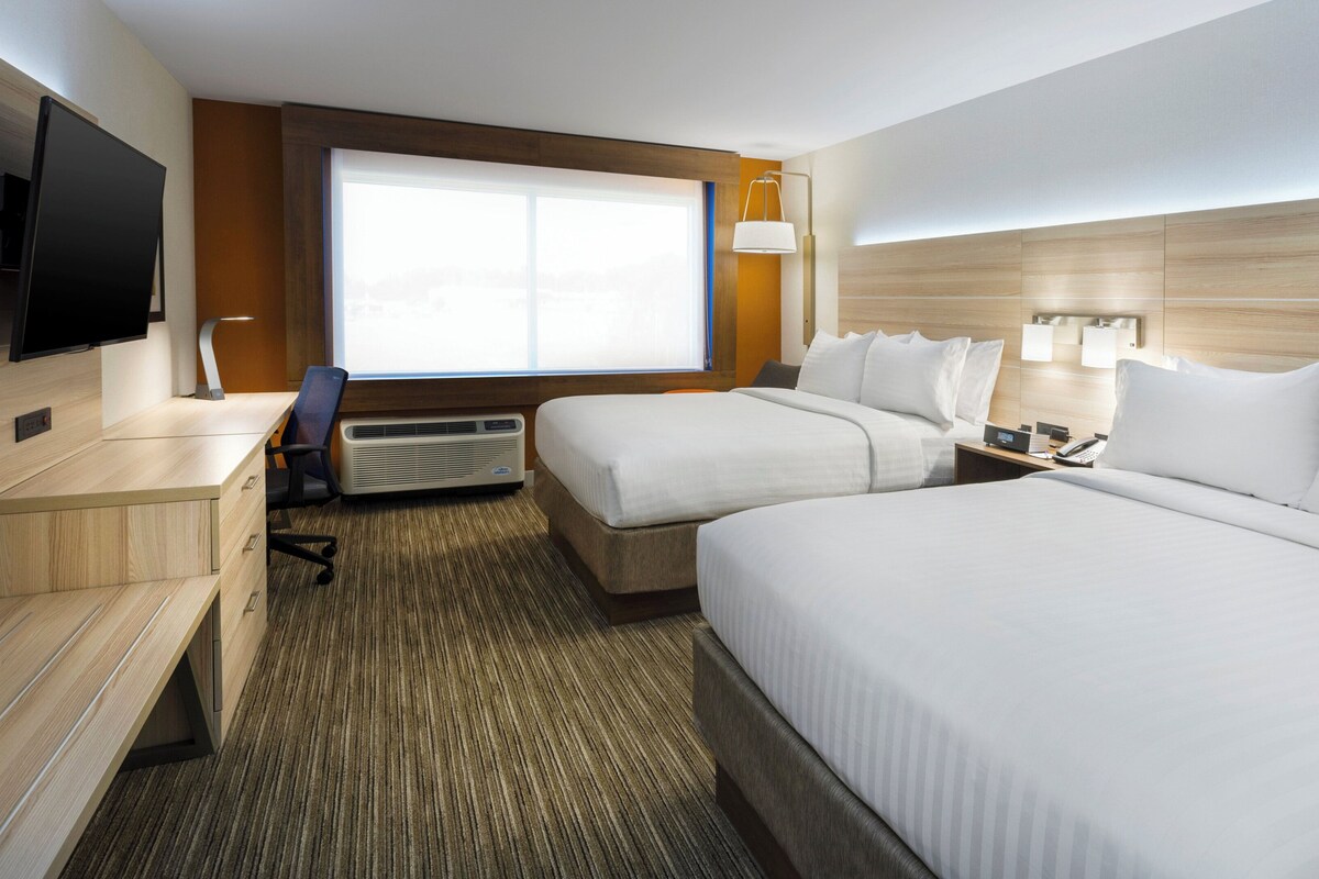 Een hotelkamer met twee bedden, een bureau, een stoel, een televisie, een verwarming en een raam.