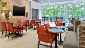 A modern dining area with red chairs and tables, a flat-screen TV, and large windows with a view of greenery. - Holiday Inn Express & Suites Medina by IHG (Medina)