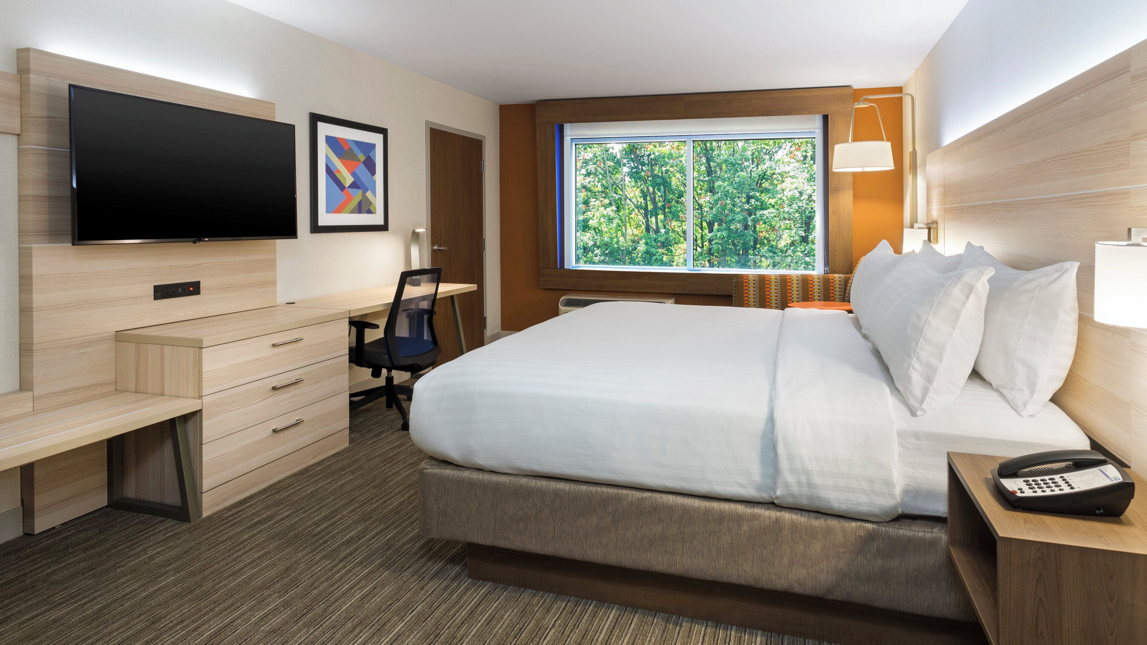 A hotel room with a bed, desk, chair, TV, and a window with a view of trees.