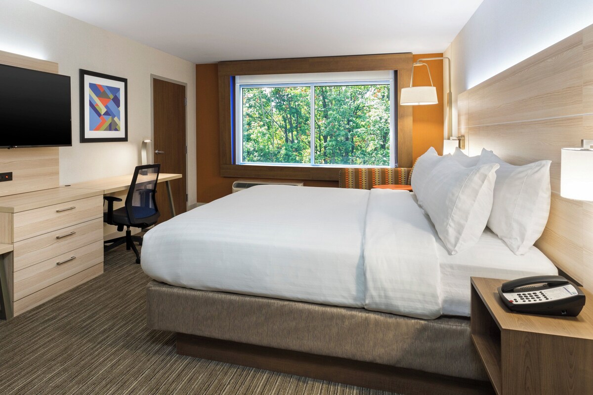 Een hotelkamer met een bed, bureau, stoel, televisie en raam met uitzicht op bomen.