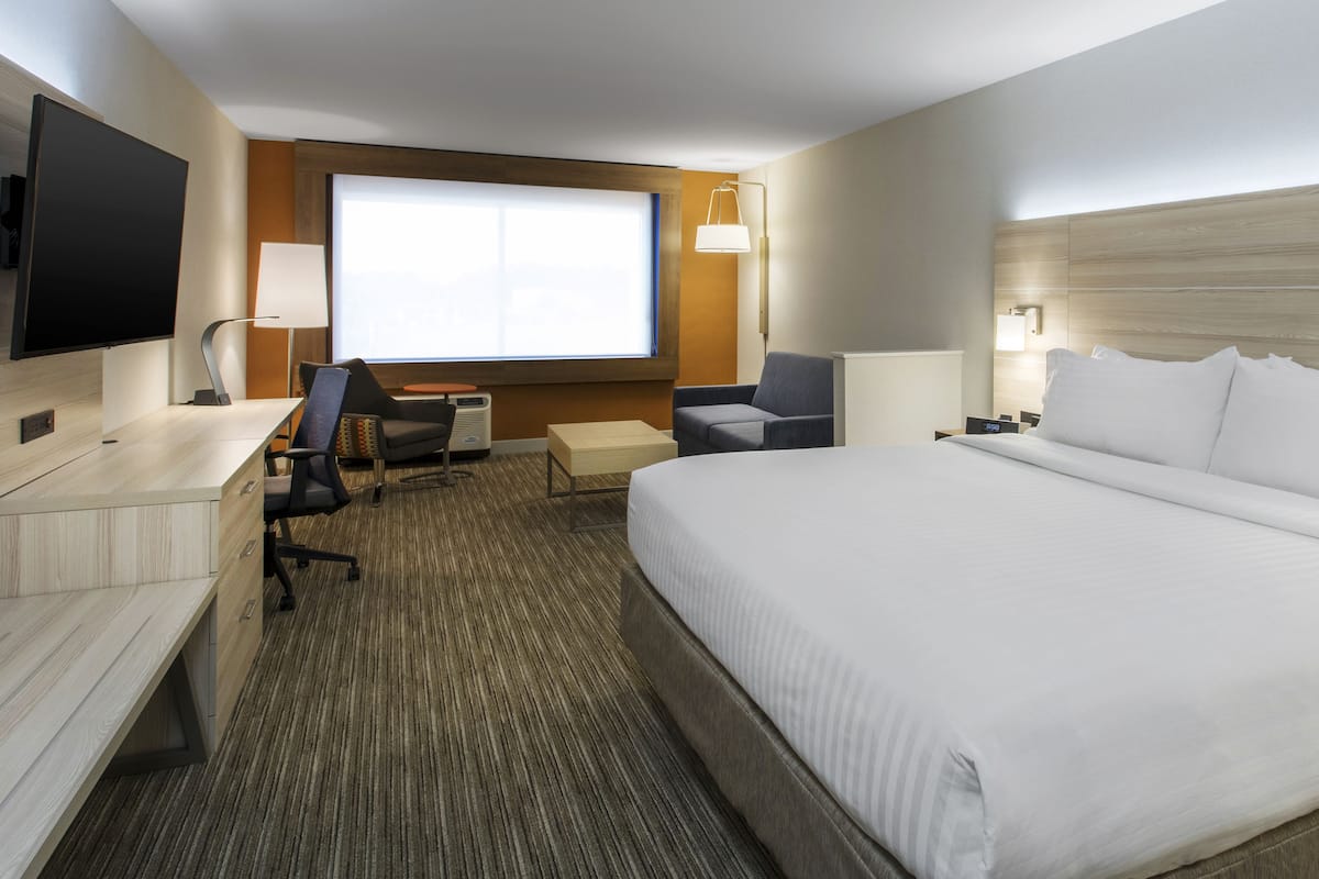 Quarto de hotel com uma cama grande, uma escrivaninha com cadeira, televisão e janela com vista.