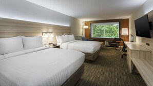 Ein Hotelzimmer mit zwei Betten, einem Schreibtisch, einem Stuhl, einem Fernseher und einem Fenster mit Blick auf Bäume.