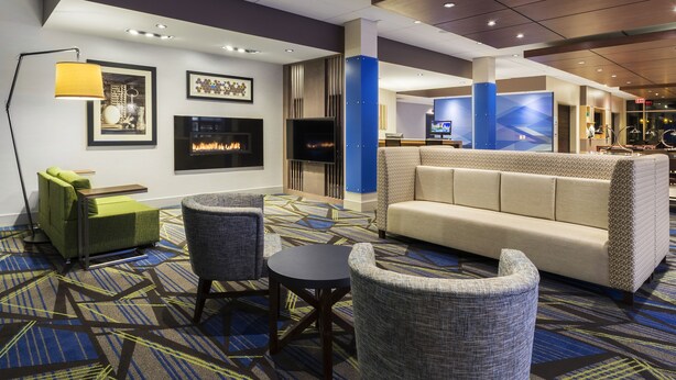 Eine Lobby mit einer Couch, Sesseln, einem kleinen Tisch, einer Stehlampe, einem Kamin und einem Fernsehbildschirm.