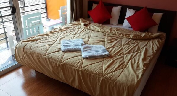 Un lit avec une couette beige, deux serviettes pliées et des oreillers rouges et blancs.