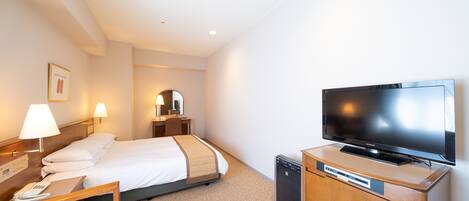 A hotel room with a bed, bedside table, lamp, TV, and a small cabinet.