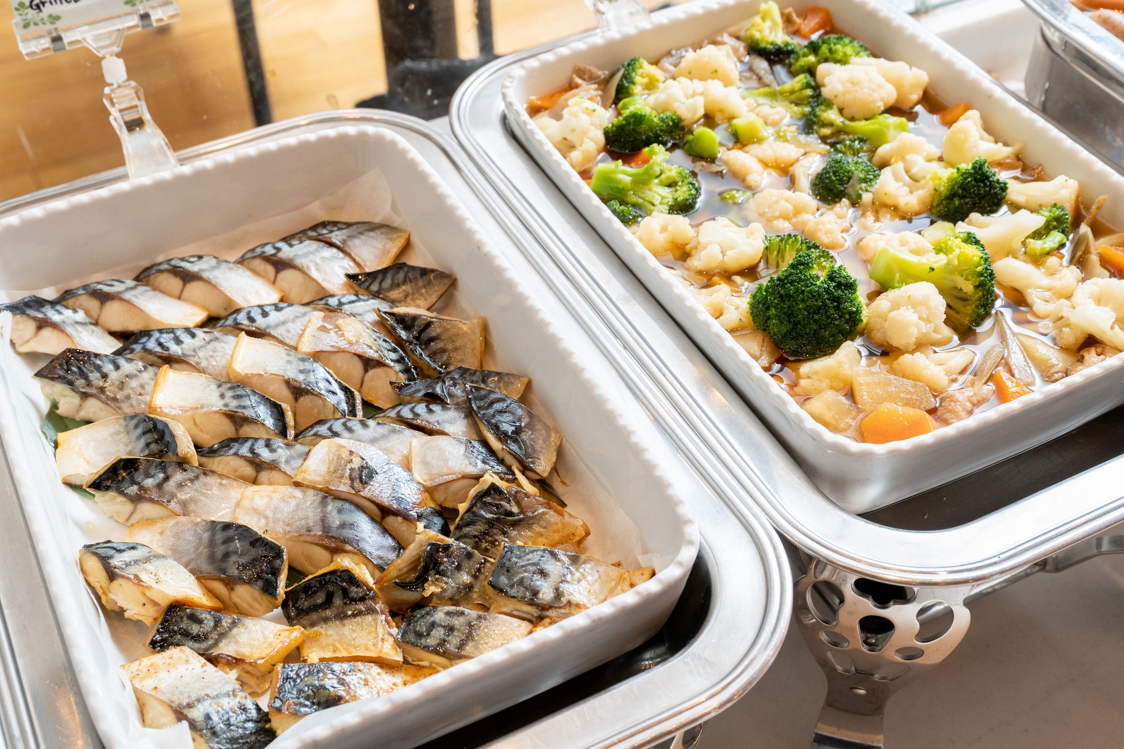 Two food trays with grilled fish and vegetables.