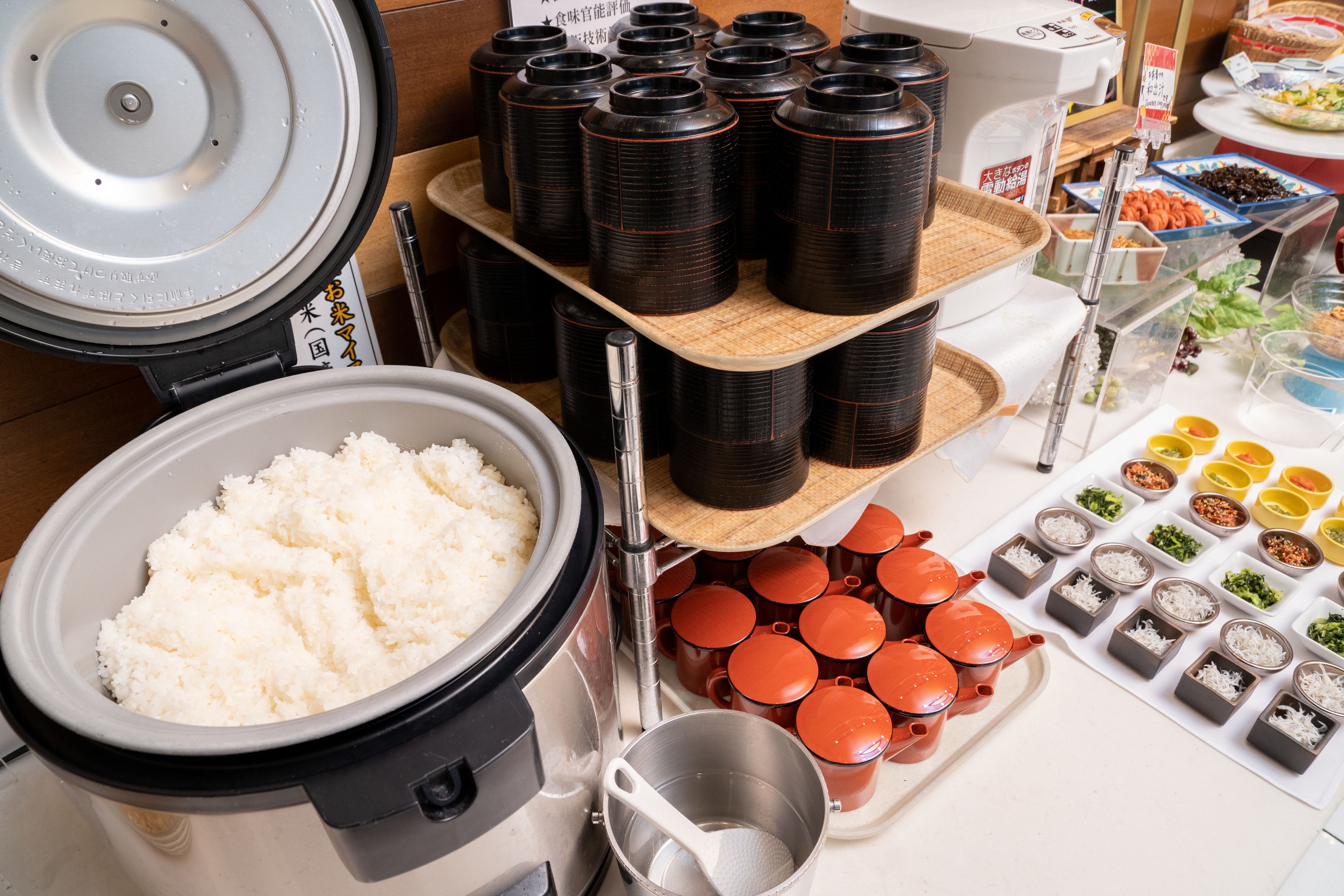 A kitchen area with a rice cooker, multiple containers, and various food items.