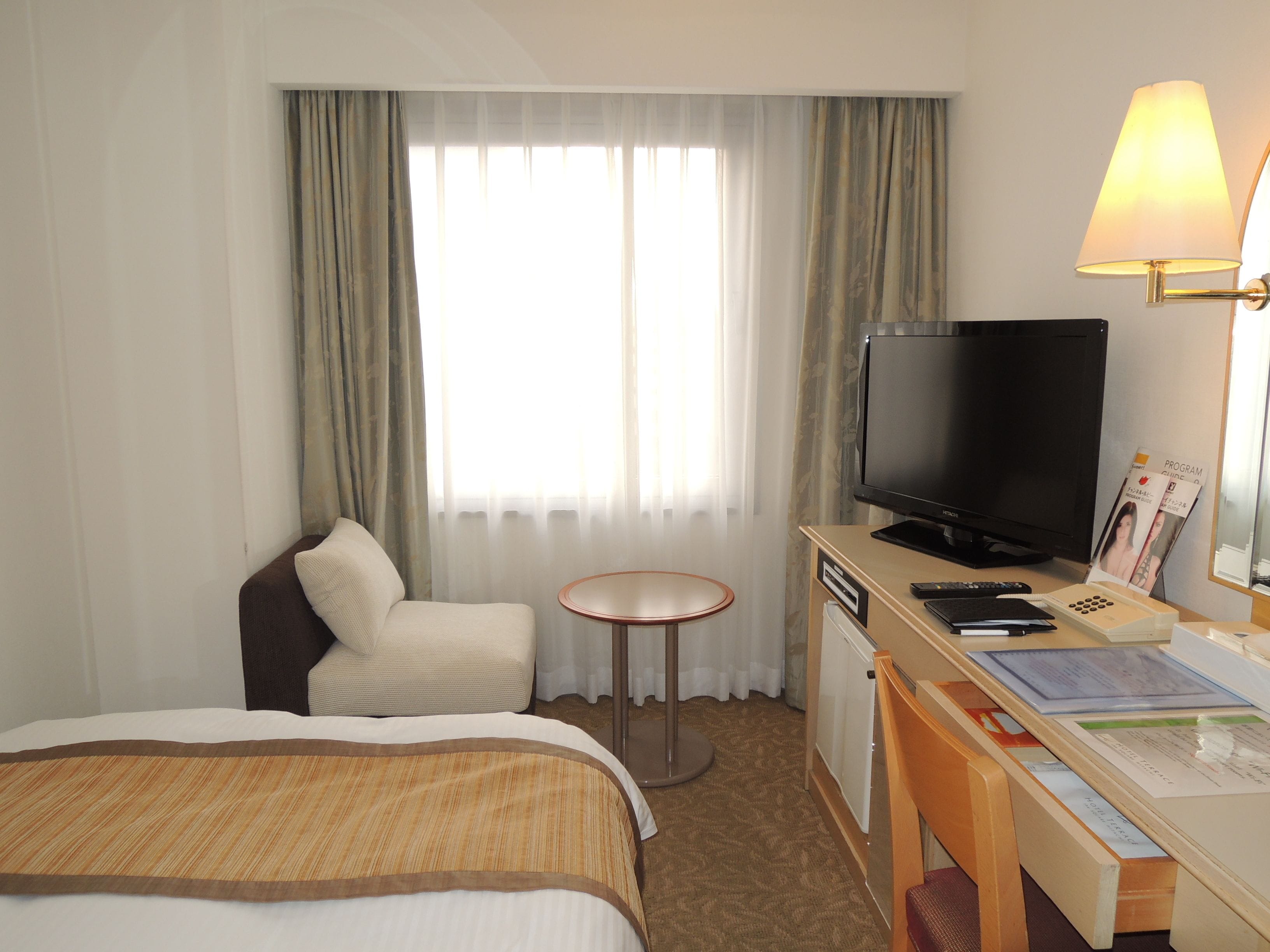 A hotel room with a bed, a desk with a computer, a television, and a chair.