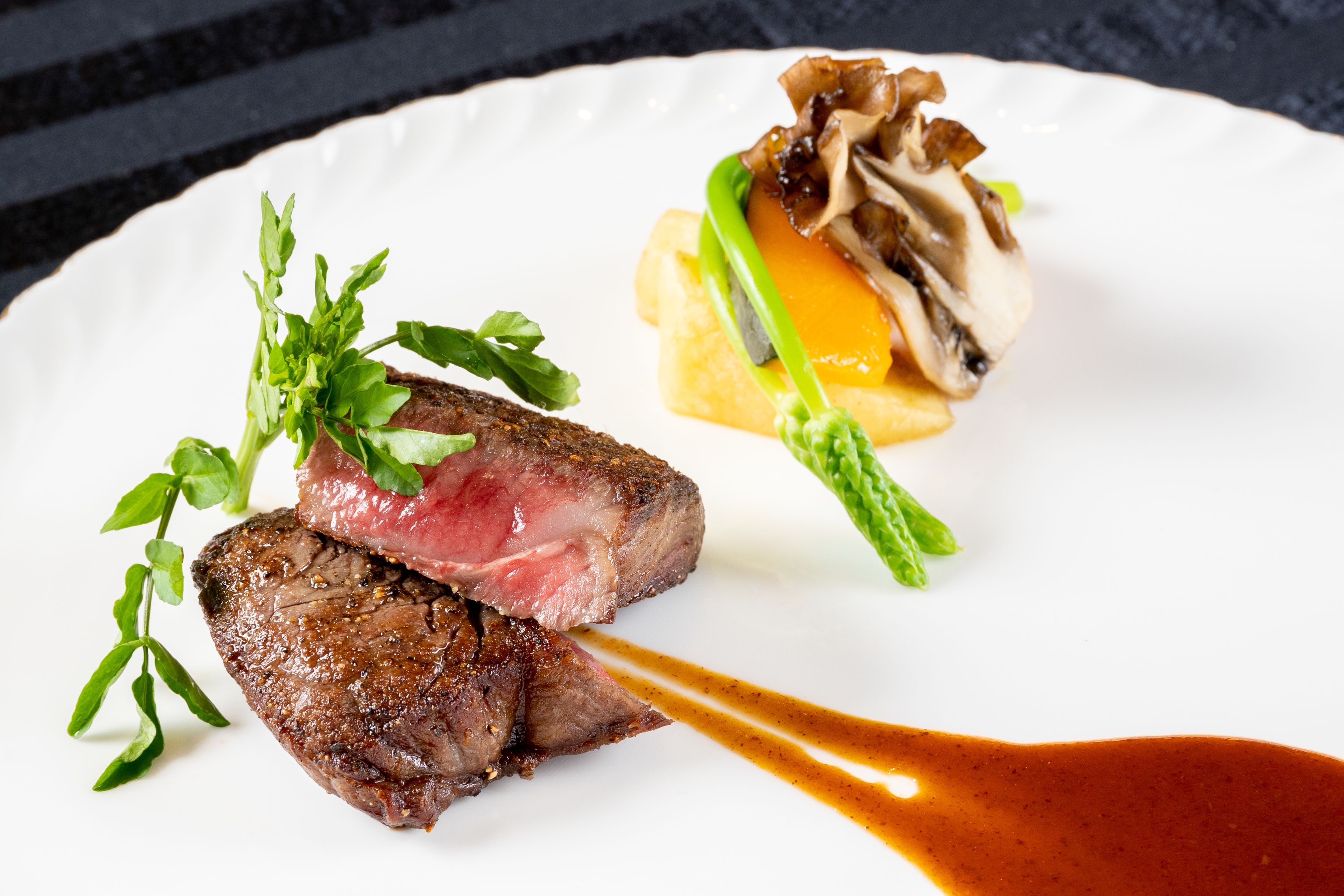 Une assiette comprenant un steak, des asperges et un plat aux champignons.