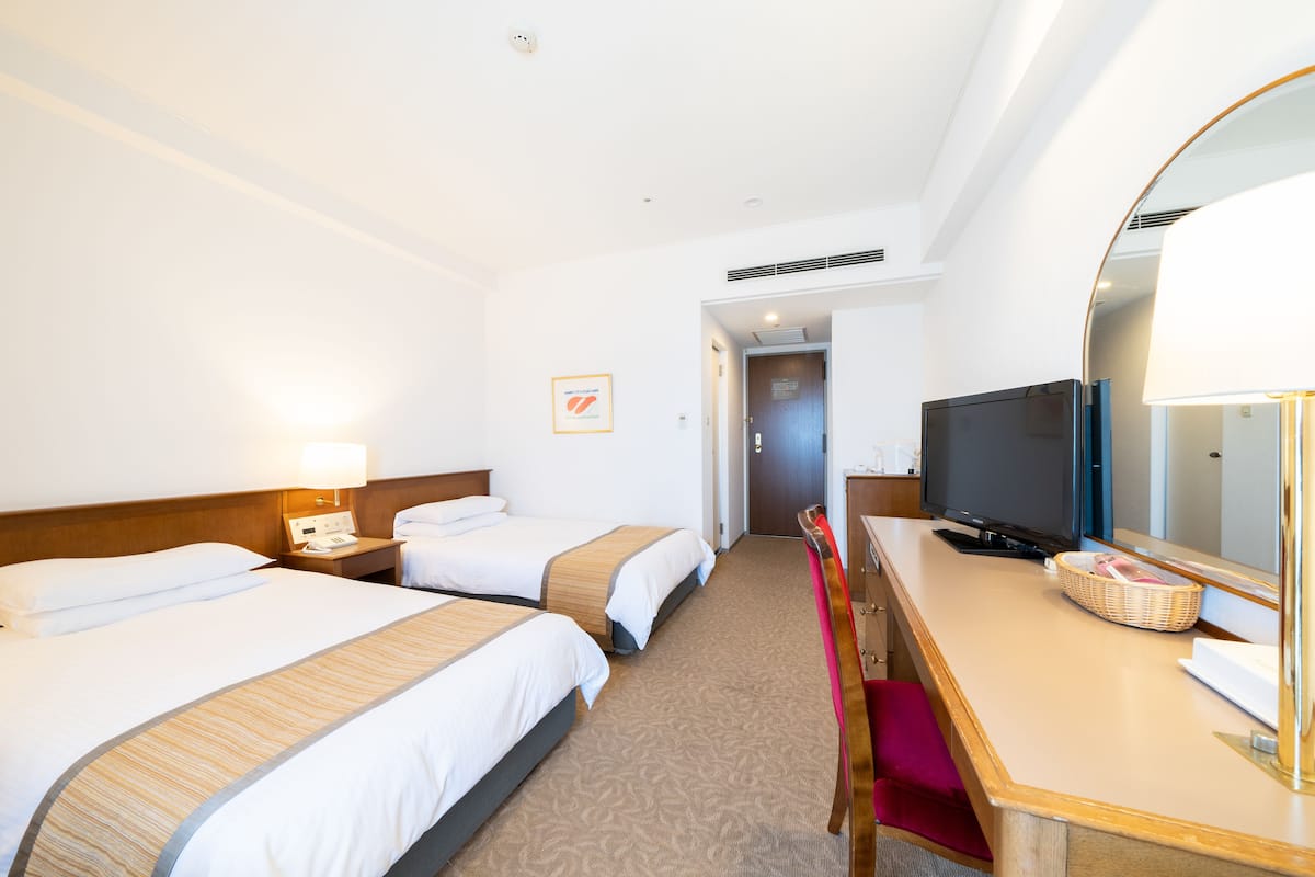 A hotel room with two beds, a desk with a television, a mirror, and a door leading to a hallway.