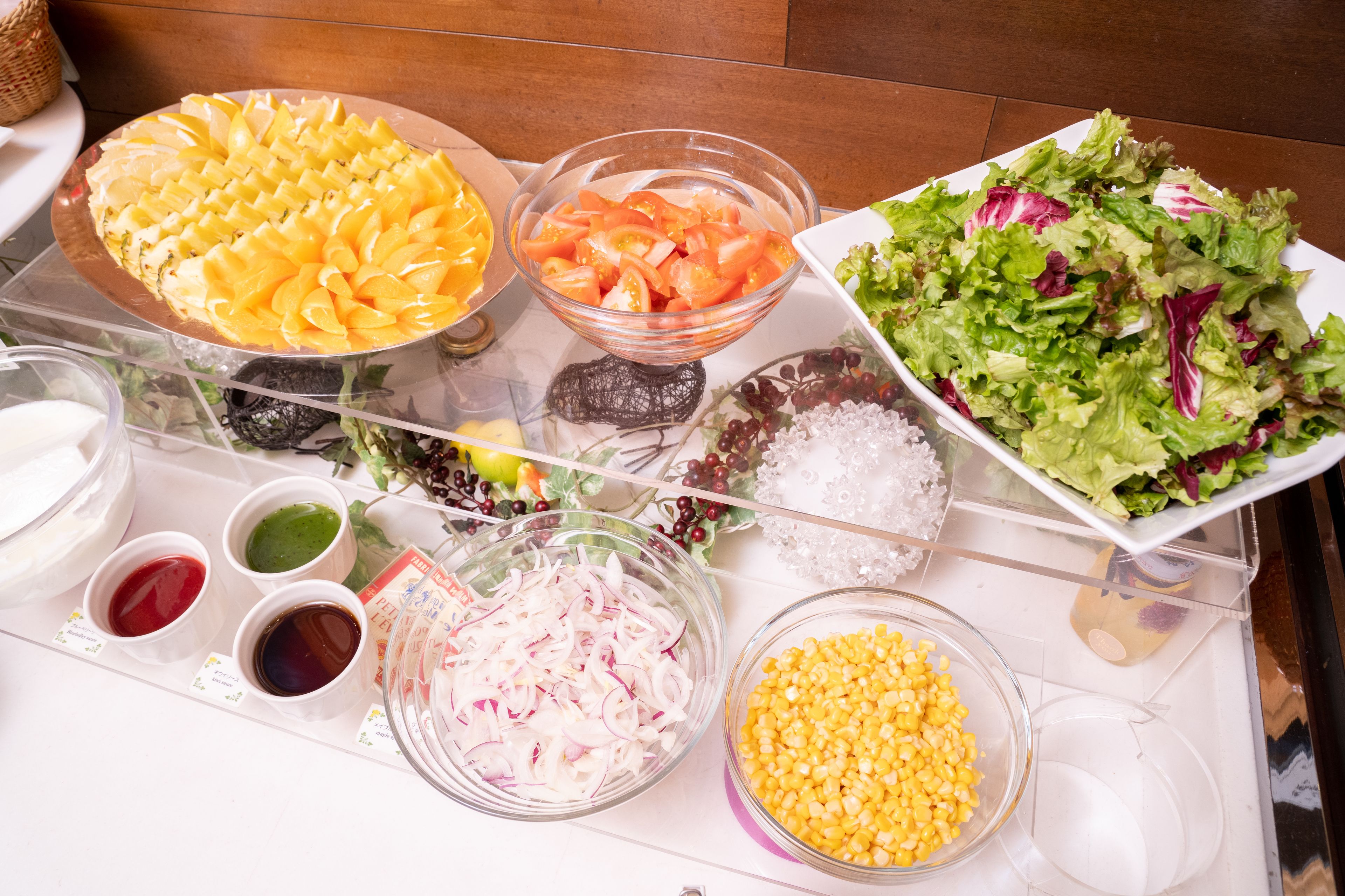 A buffet table with various food items including a fruit platter, salad, and bowls of corn and onions.