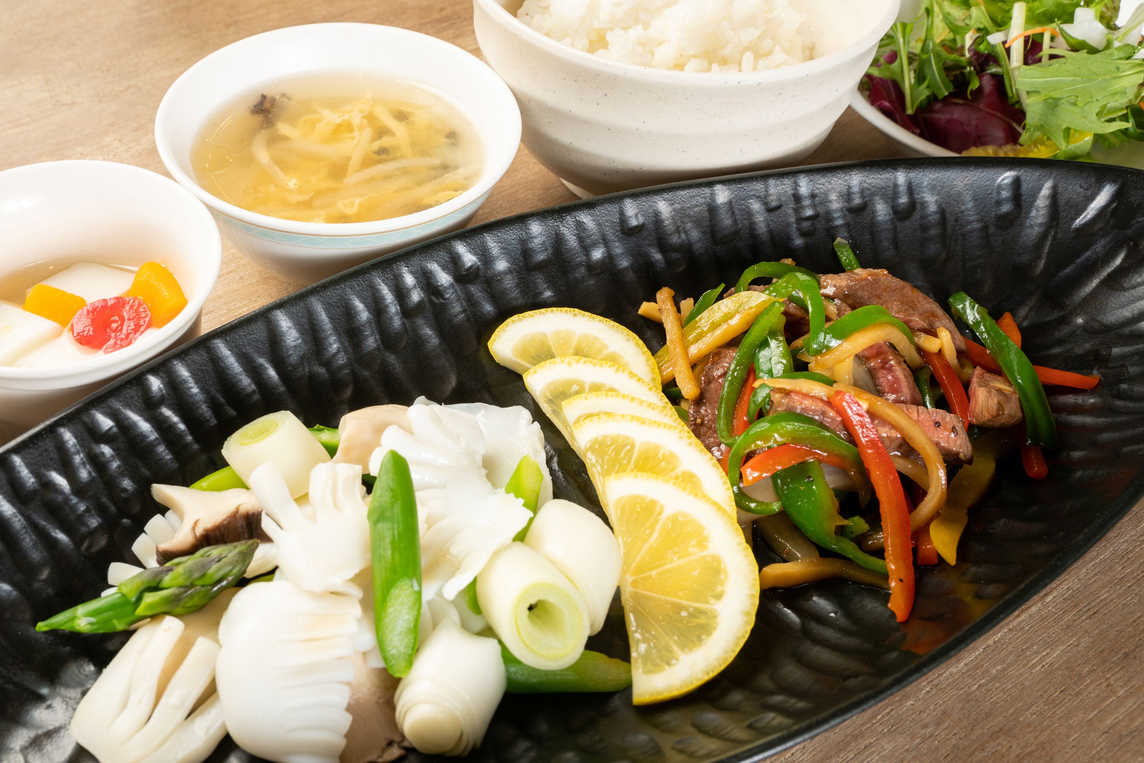 A meal with various dishes including a bowl of soup, a plate of stir-fried vegetables, and a bowl of rice.