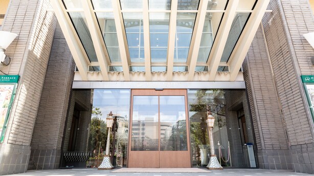 A building entrance with a large glass door, brick walls, and a decorative canopy. - Hotel Terrace The Square Hitachi (Hitachi)