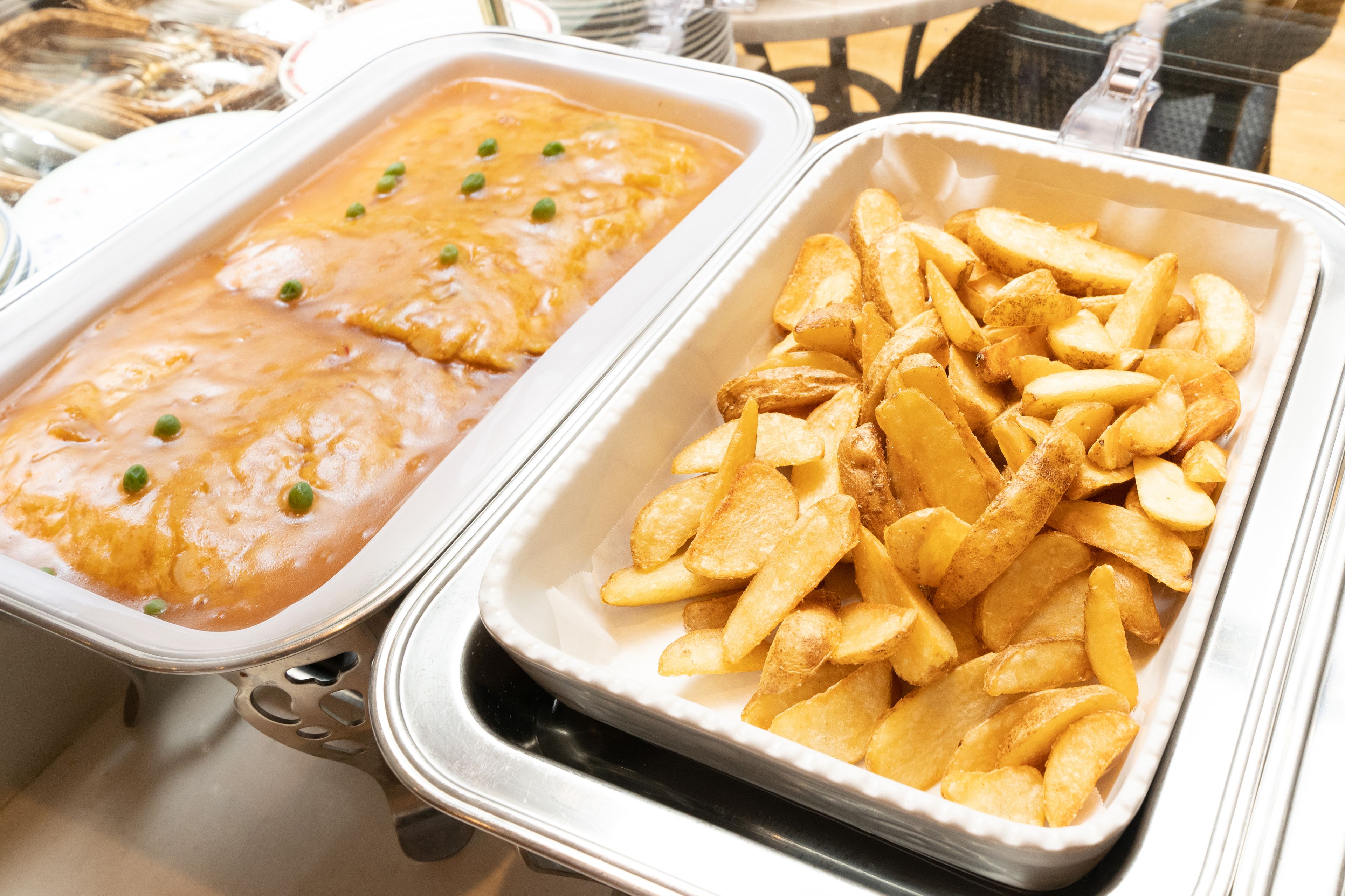 A buffet with two dishes: a creamy casserole with peas and a tray of golden-brown potato wedges.