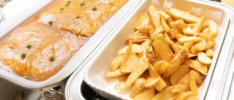 A buffet with two dishes: a creamy casserole with peas and a tray of golden-brown potato wedges.