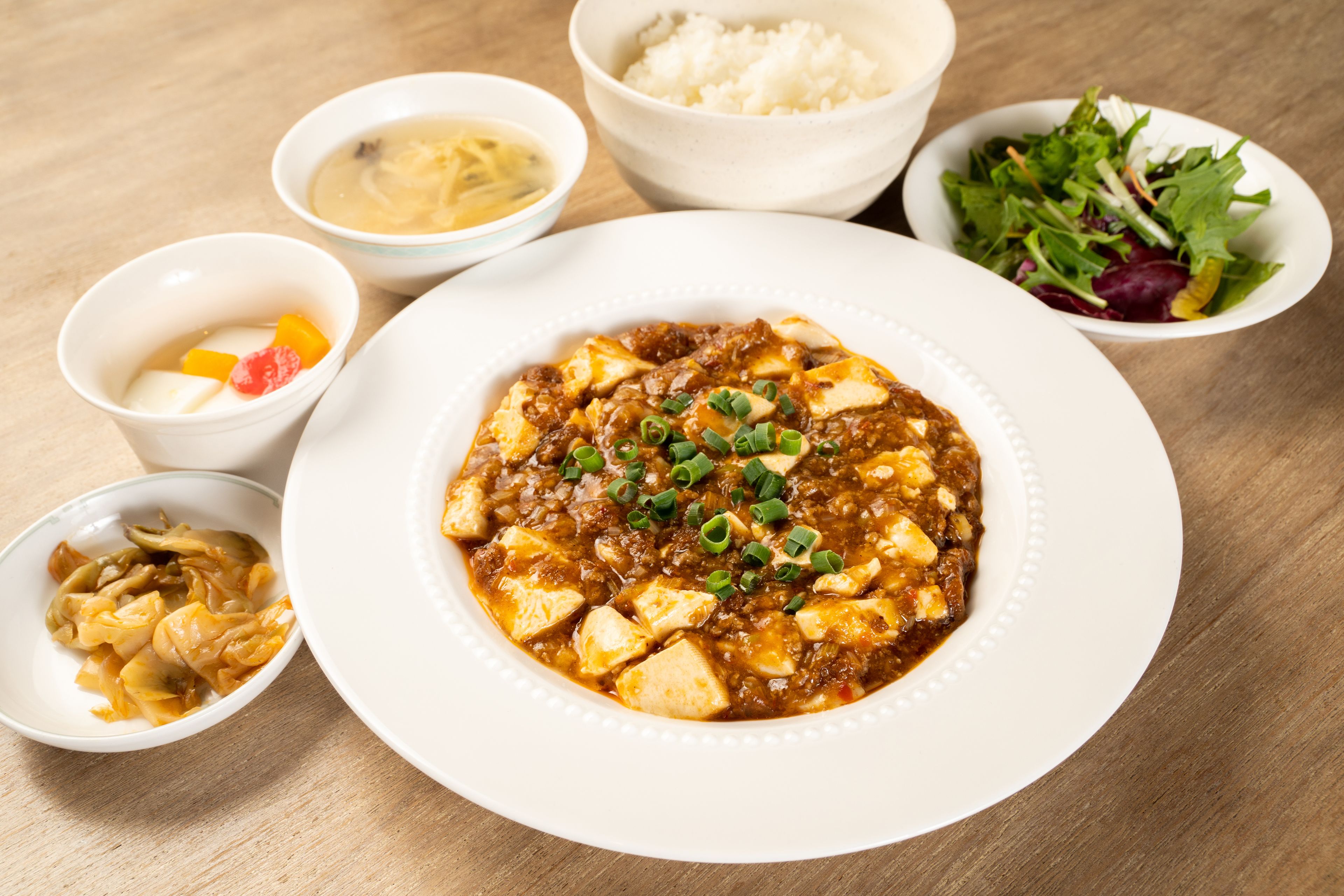 A table with various dishes including a bowl of soup, a plate of tofu, and a salad.