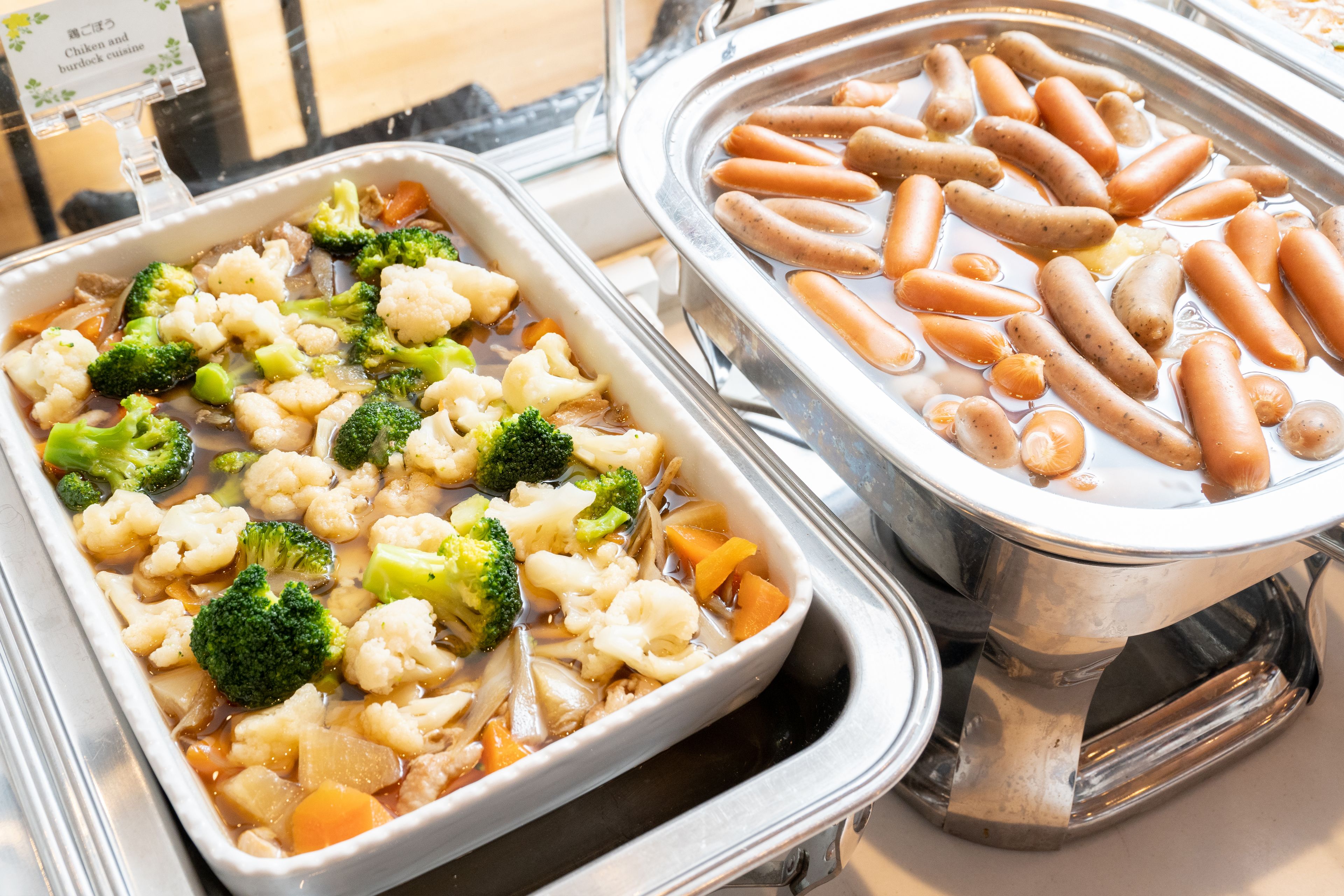 A buffet with a variety of dishes including vegetables and sausages.